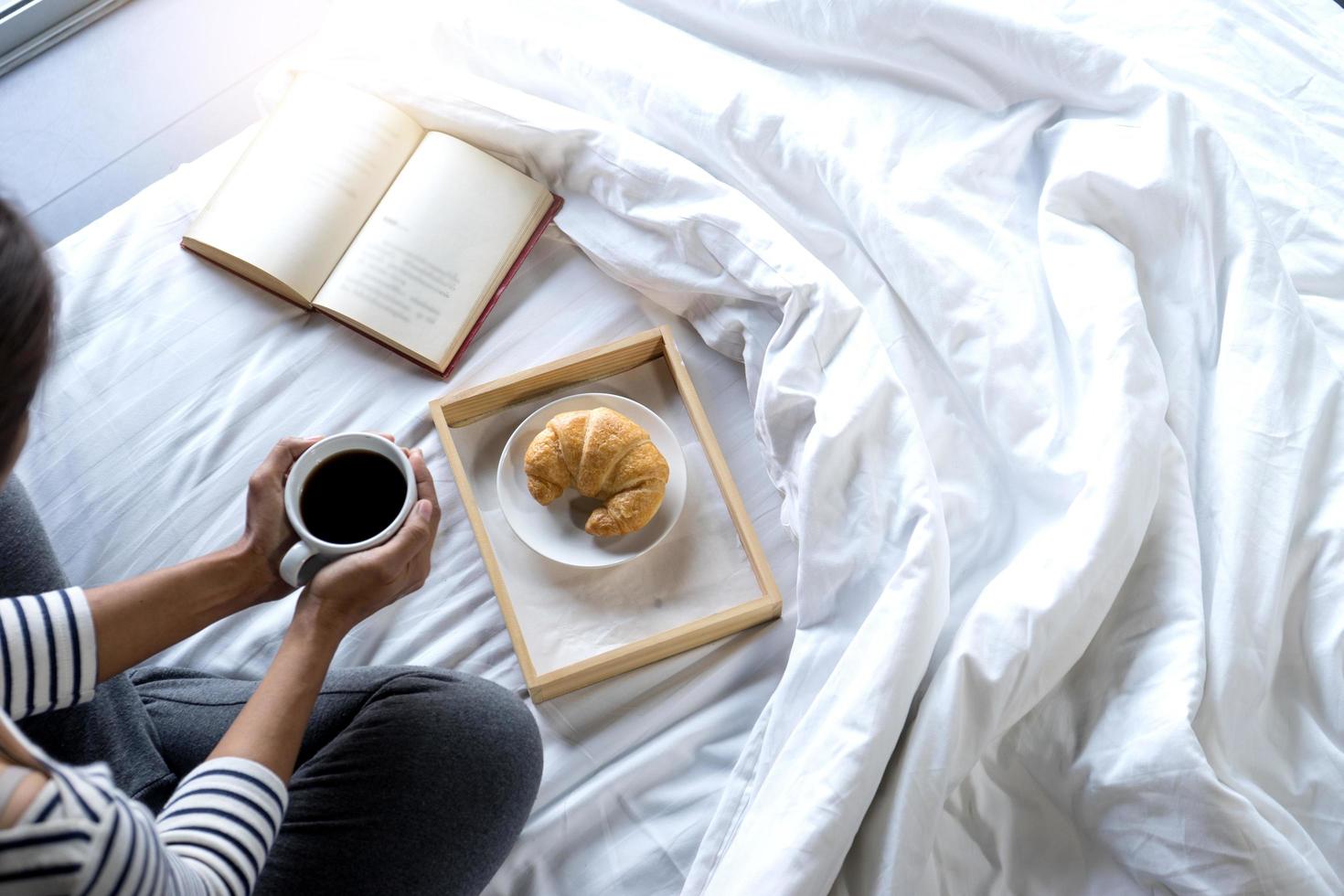 Frau entspannt auf dem Bett mit Buch und Frühstück foto