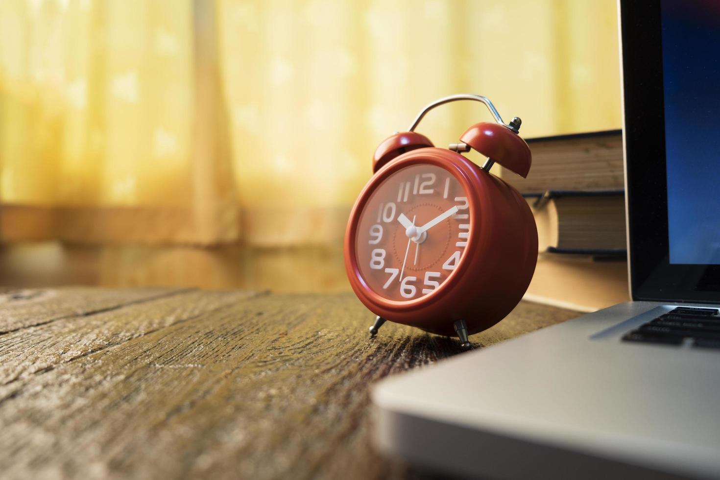 Vintage rote Uhr und Laptop auf Holztisch foto