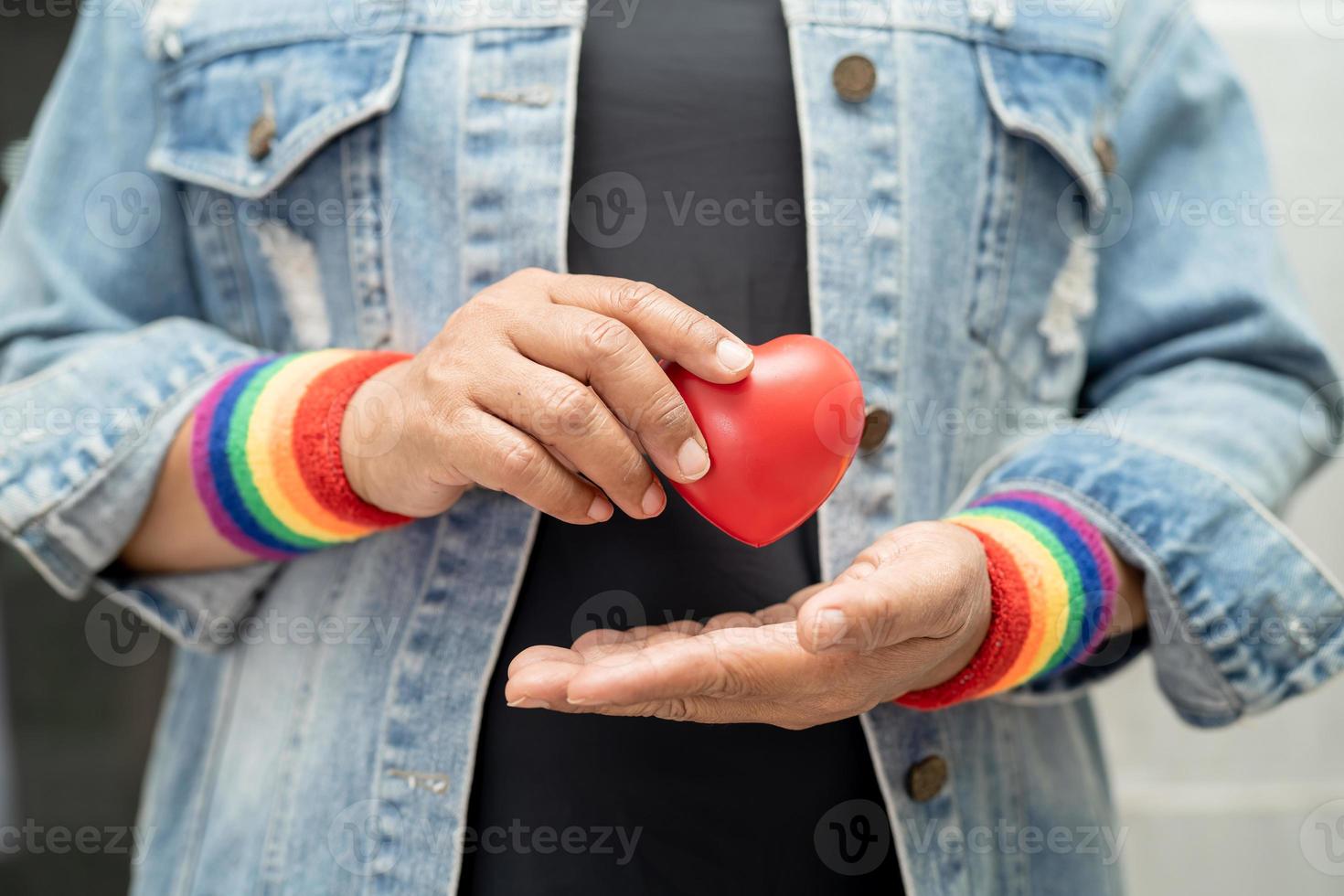 asiatische dame, die regenbogenflaggenarmbänder trägt und rotes herz hält, symbol des lgbt-stolzmonats, feiert jährlich im juni sozial für schwule, lesbische, bisexuelle, transgender, menschenrechte. foto