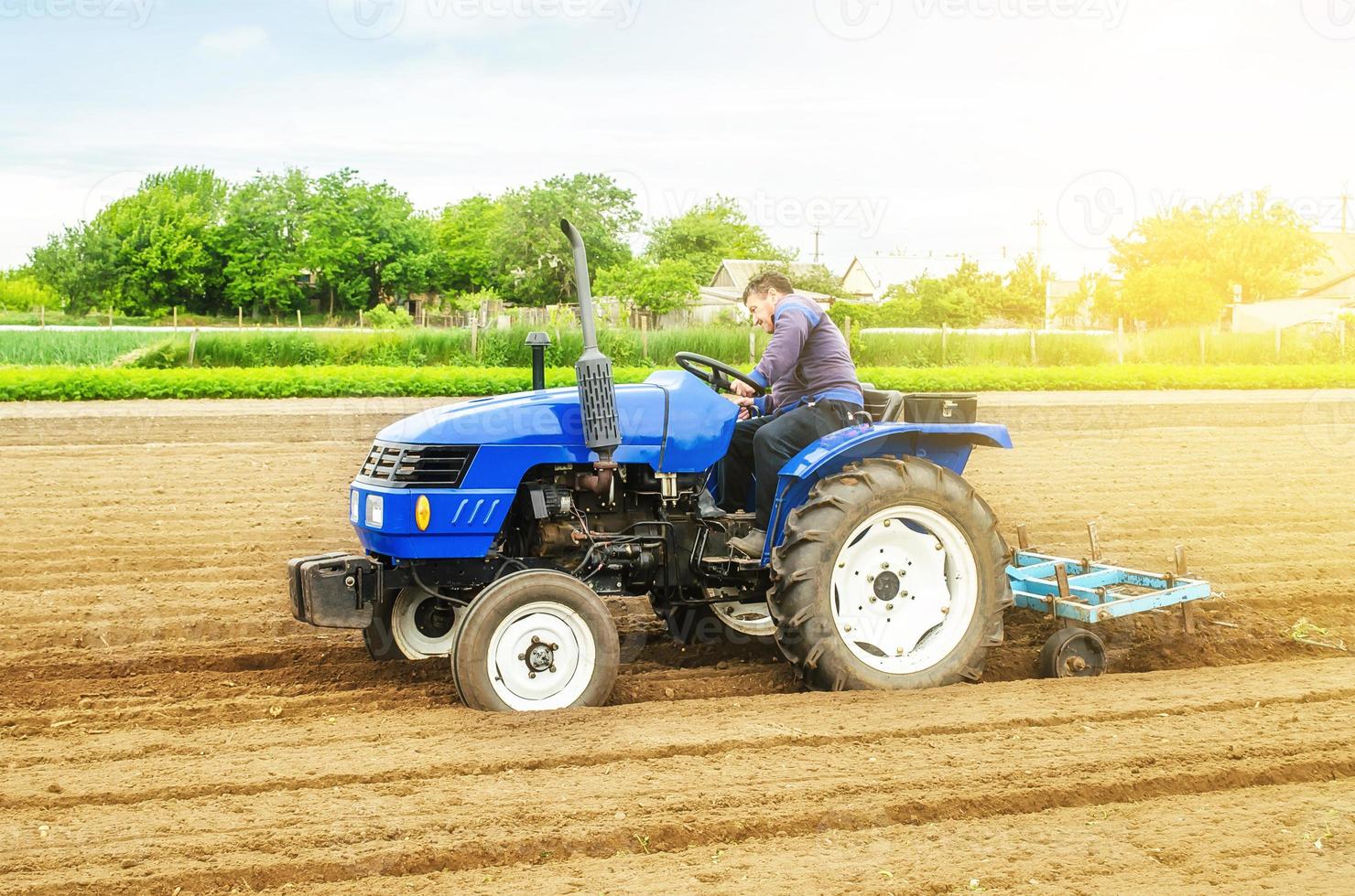 ein weißer kaukasischer Bauer auf einem Traktor, der Grate und Hügelreihen auf einem Bauernhoffeld macht. Vorbereitung des Bodens für die Anpflanzung zukünftiger Kulturpflanzen. Kultivierung von Erde für Pflanzzwecke. Agrarindustrie, Agrarindustrie. foto