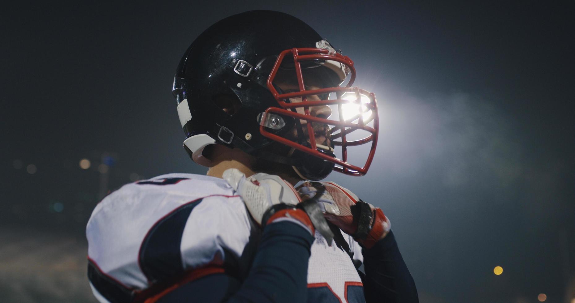 American-Football-Spieler, der einen Helm auf einem großen Stadion mit Lichtern im Hintergrund aufsetzt foto