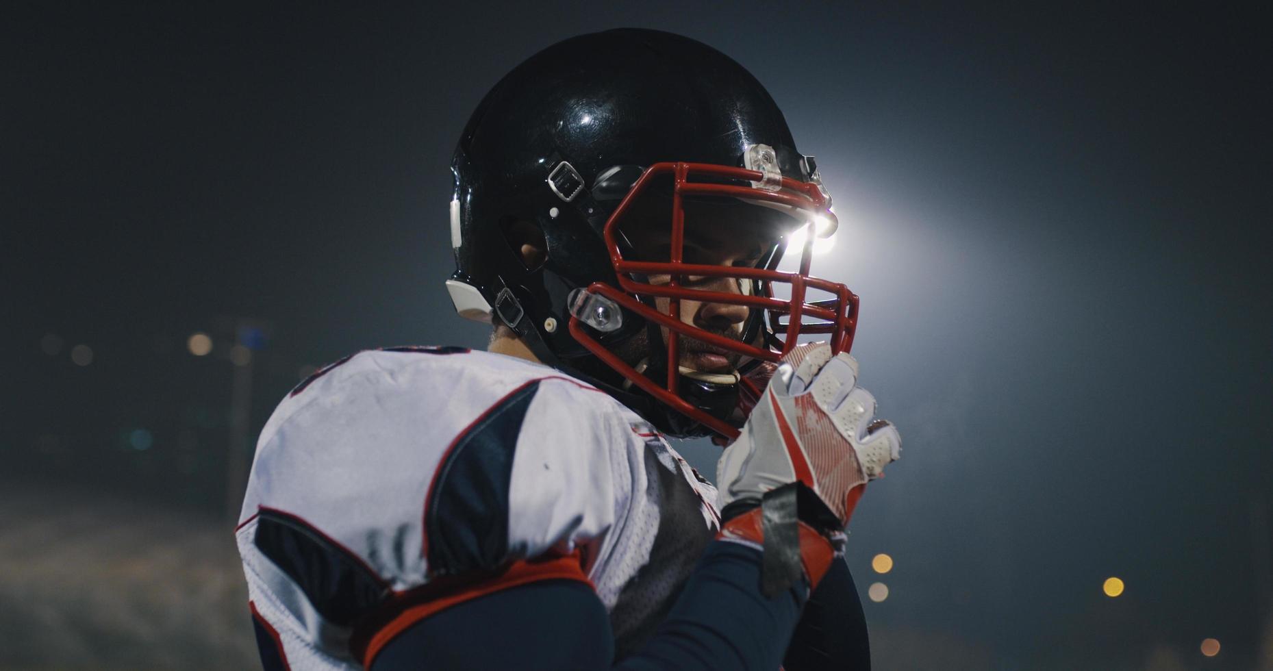 American-Football-Spieler, der einen Helm auf einem großen Stadion mit Lichtern im Hintergrund aufsetzt foto