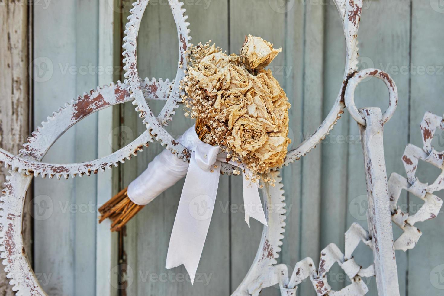 Strauß getrockneter Rosen, gebunden mit weißem Band, in Tür aus Metallzahnrädern foto