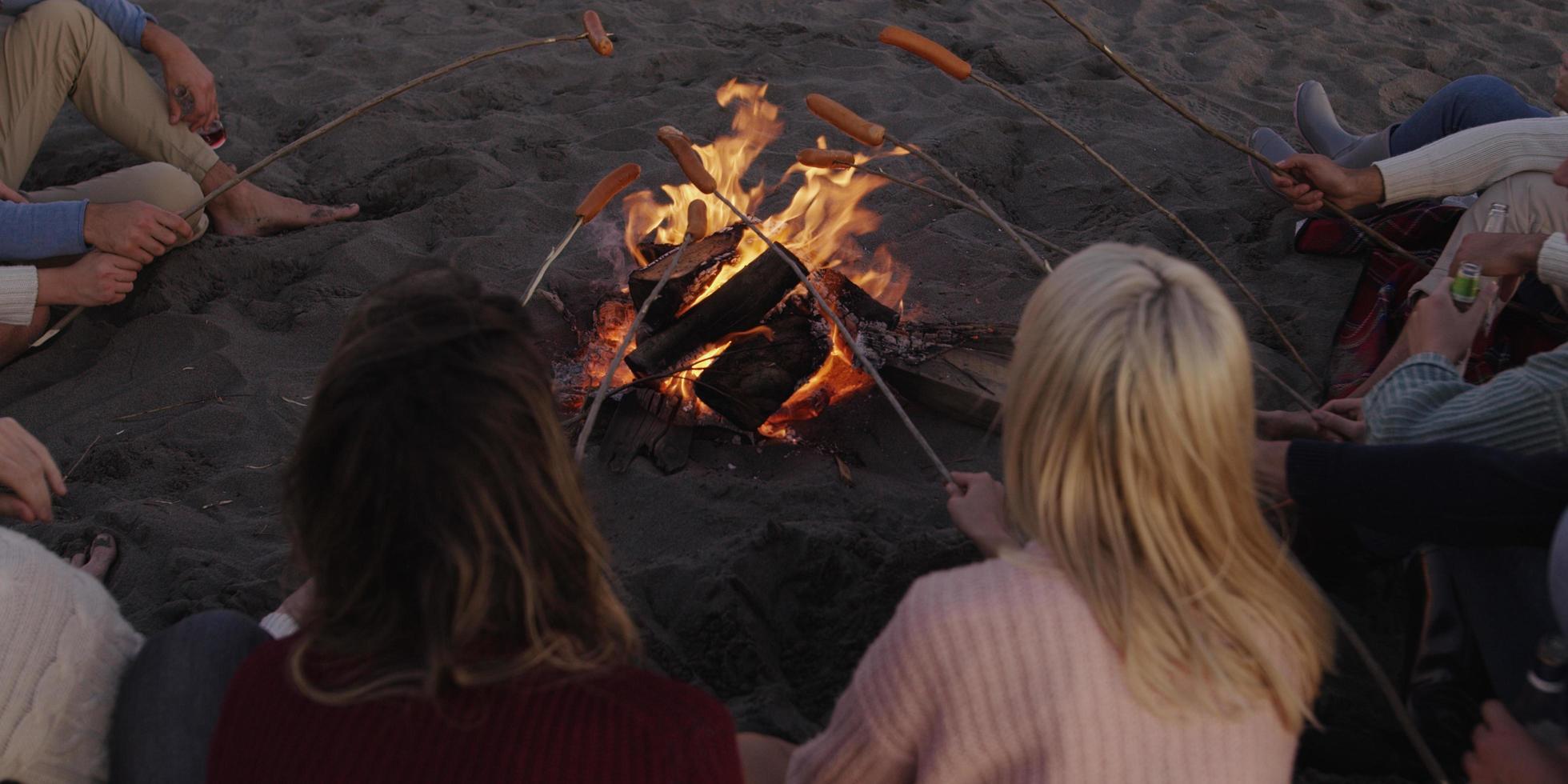 Gruppe junger Freunde, die am Feuer am Strand sitzen foto