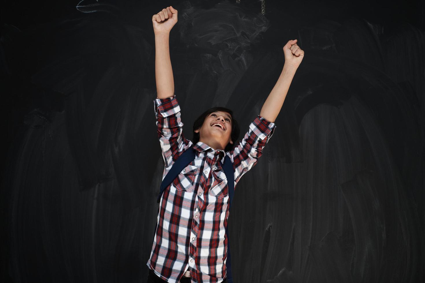glücklicher arabischer Teenager, der gegen schwarze Tafel feiert foto