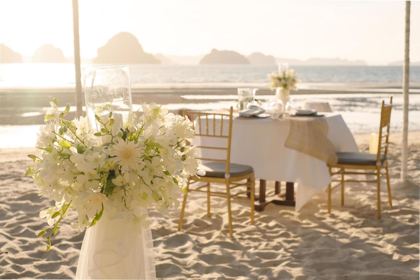 Schöner Tisch für ein romantisches Abendessen am Strand mit Blumen und Kerzen. Catering für ein romantisches Date, eine Hochzeit oder einen Flitterwochenhintergrund. Abendessen am Strand bei Sonnenuntergang. ausgewählten Fokus. foto