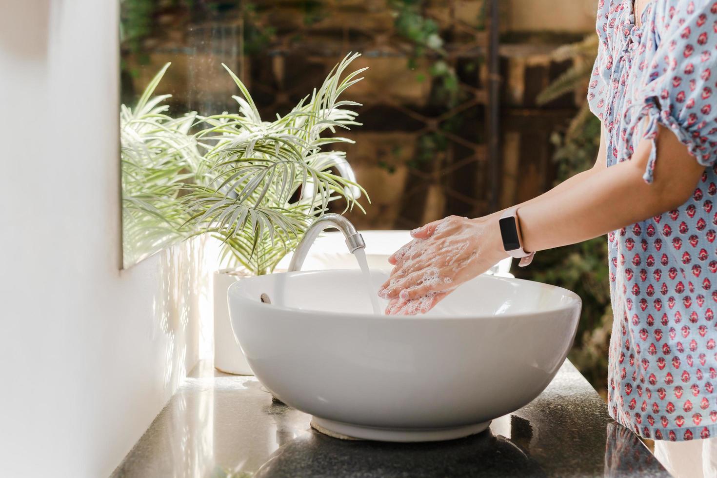 Frau wäscht sich die Hände mit Leitungswasser unter Wasserhahn am weißen Waschbecken. foto