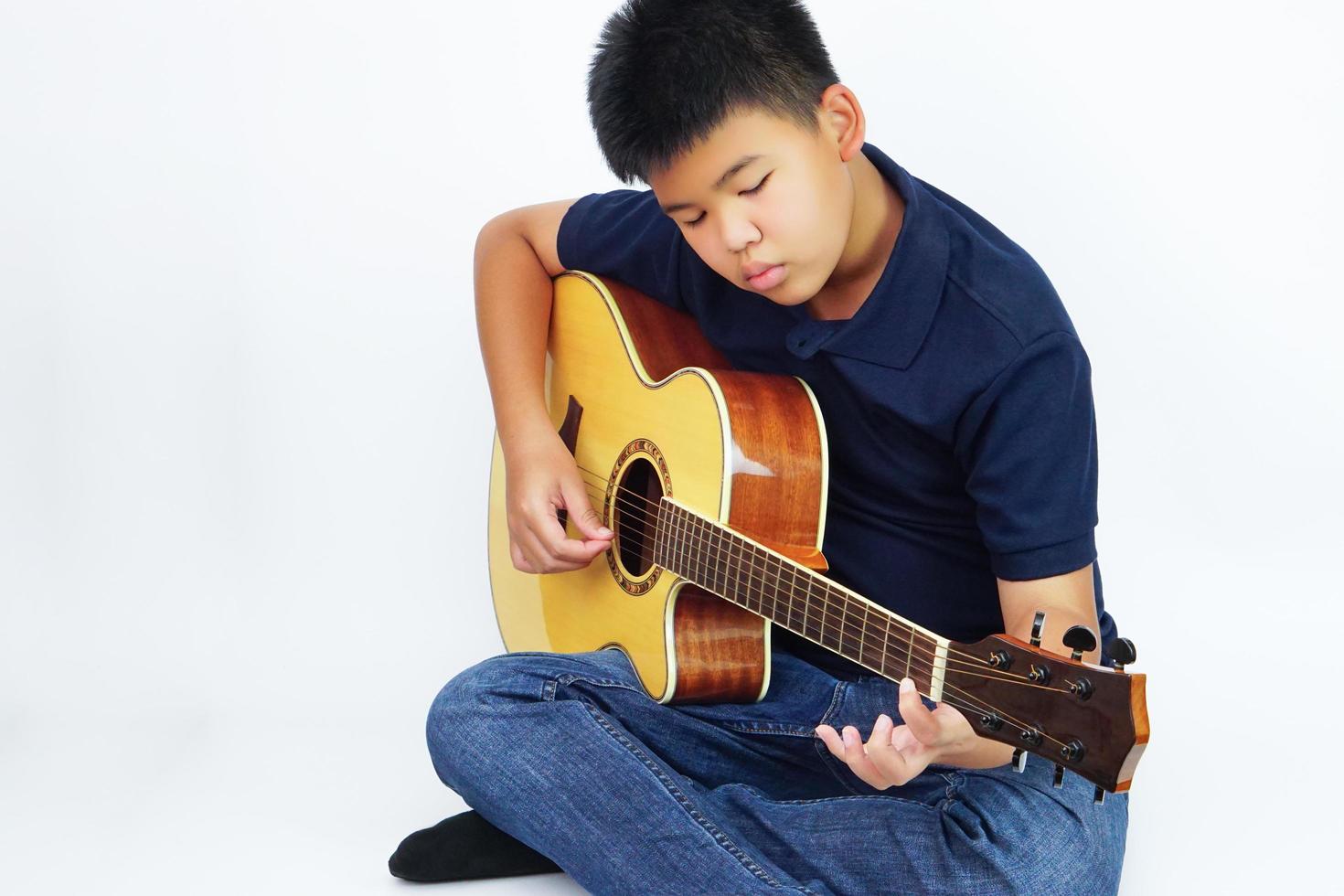 Kind oder Teenager spielt Akustikgitarre auf weißem Hintergrund. Lern- und Entspannungskonzept. foto