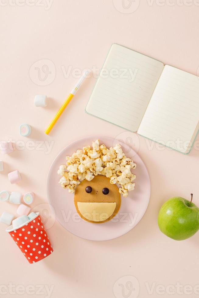 Baby-Pfannkuchen zum Frühstück. kreative idee für das kinderdessert leckere pfannkuchen in form des fröhlichen gesichts mit den haaren, die popcorn machen foto