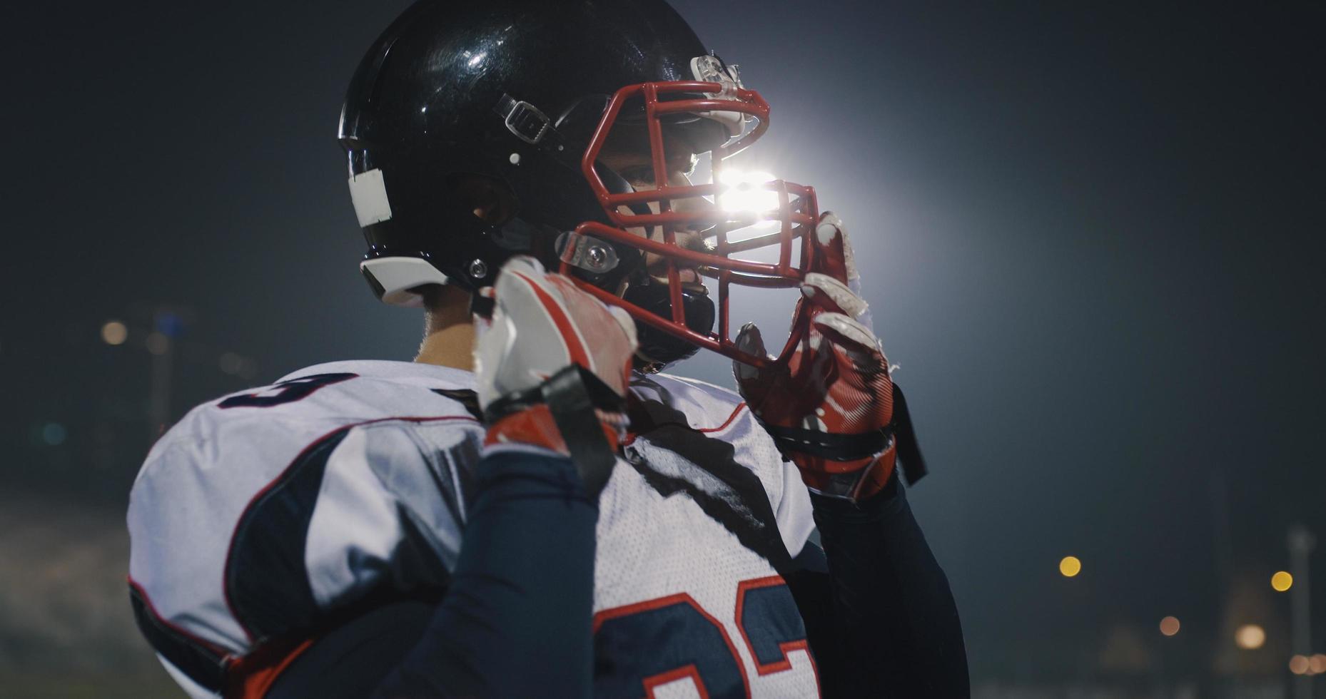 American-Football-Spieler, der einen Helm auf einem großen Stadion mit Lichtern im Hintergrund aufsetzt foto