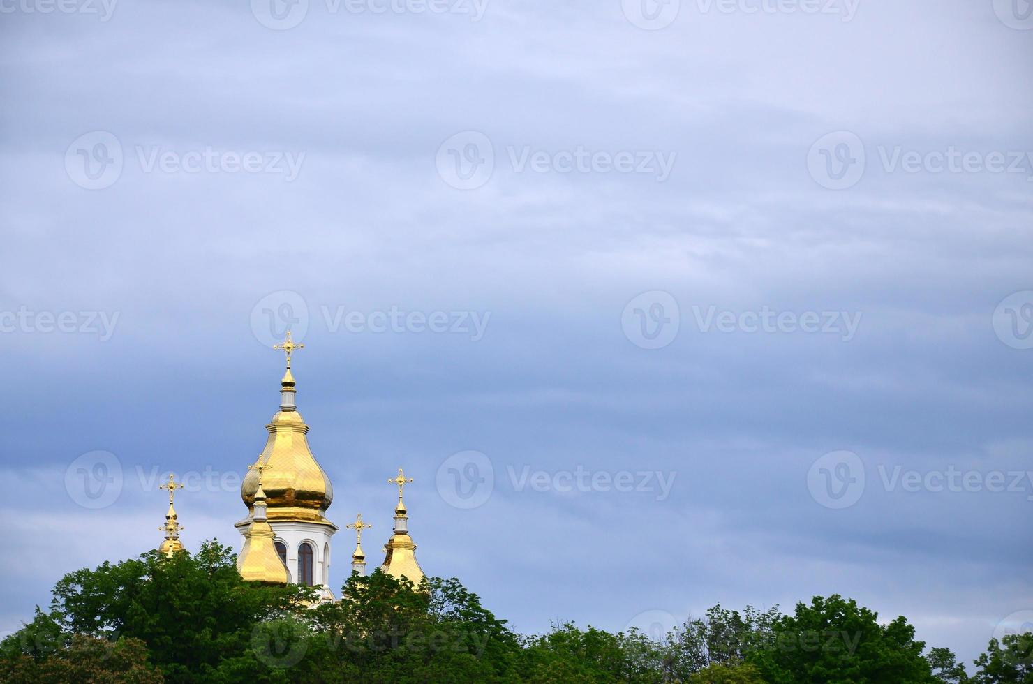 Goldene Kuppeln einer orthodoxen Kirche zwischen blühenden Bäumen vor dem Hintergrund eines wolkig blauen Himmels foto