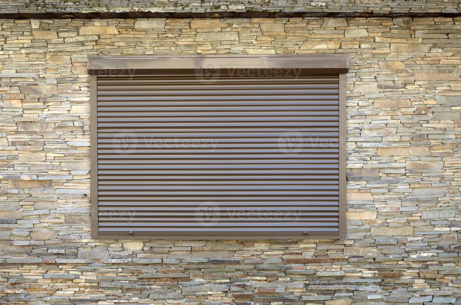 ein Fenster mit Rollläden aus braunem Metall und Wanddekoration mit Kunststein foto