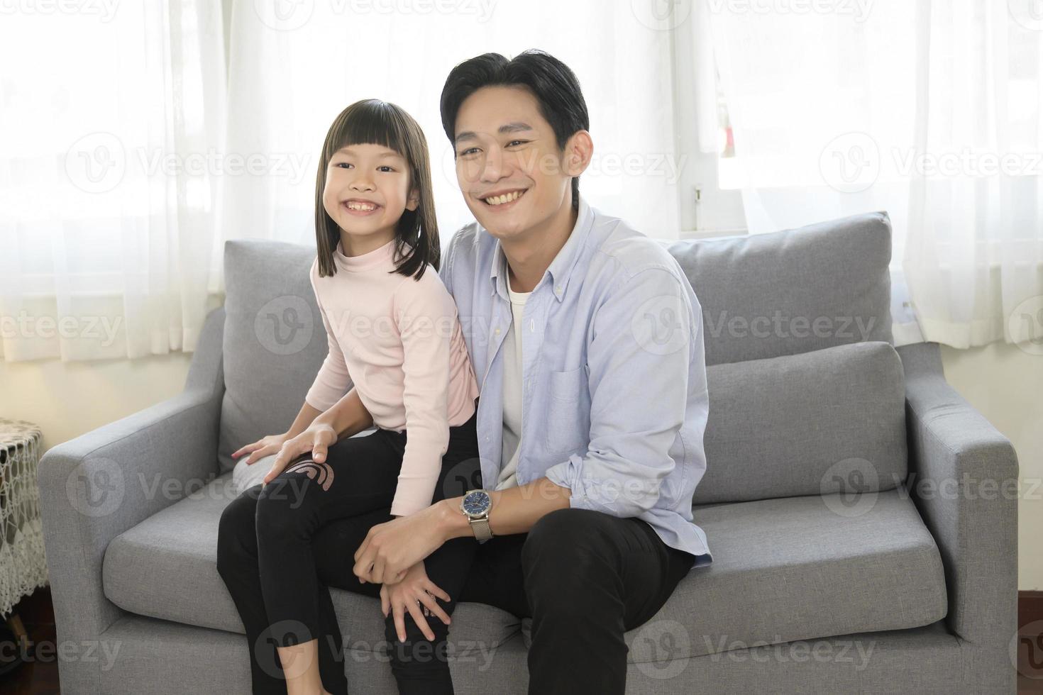 porträt des asiatischen vaters und der tochter, die auf der couch im wohnzimmer sitzen foto