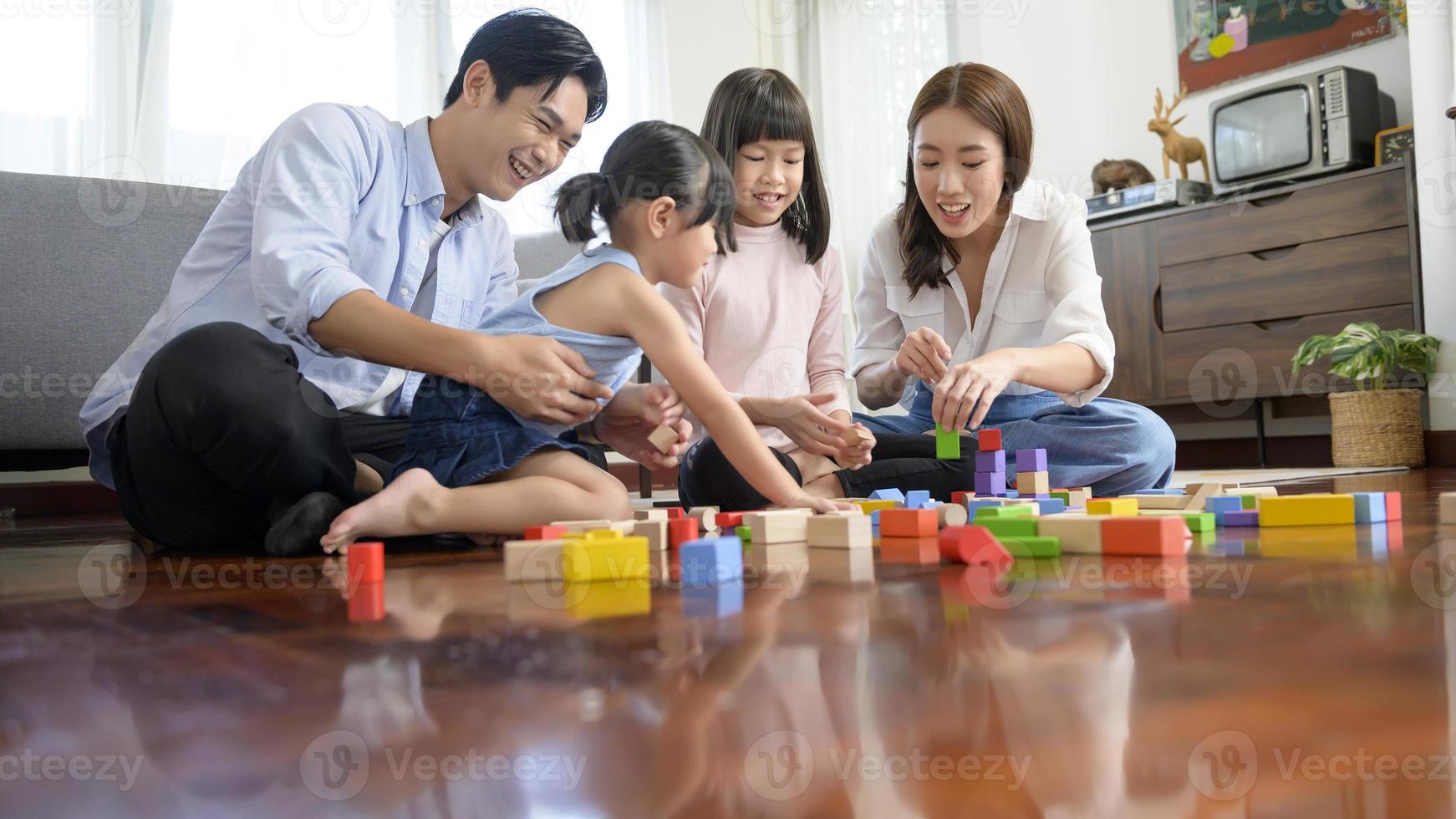 asiatische familie mit kindern, die spielen und turm aus bunten holzspielzeugblöcken im wohnzimmer zu hause bauen, lernspiel. foto