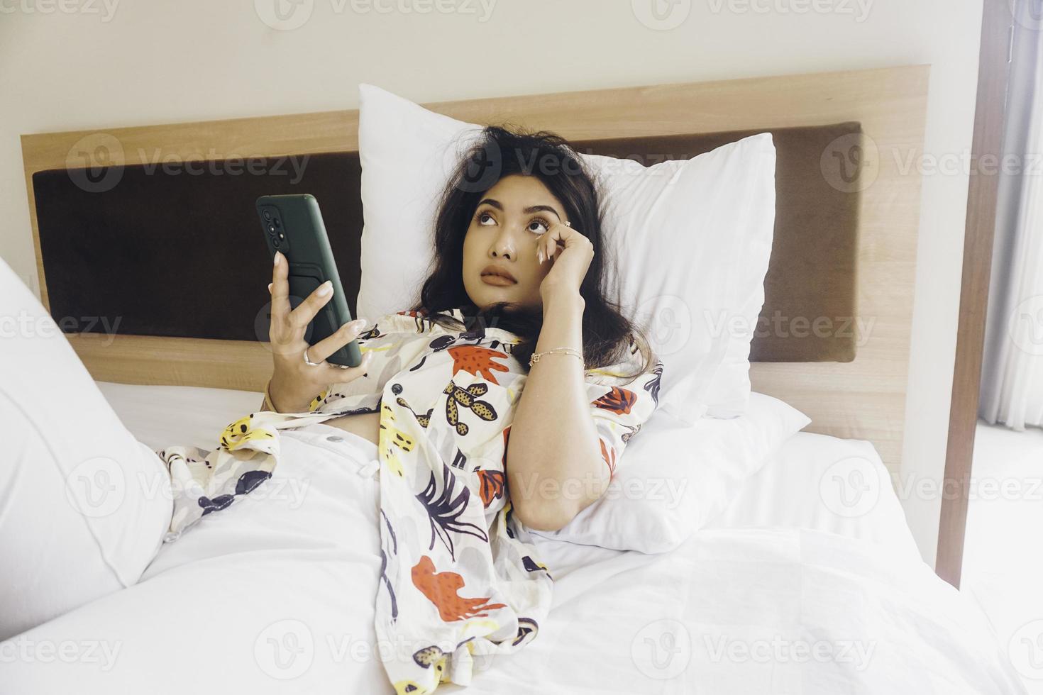 traurige junge frau, die aus dem bett weint. Halten Sie das Smartphone beim Tippen. foto