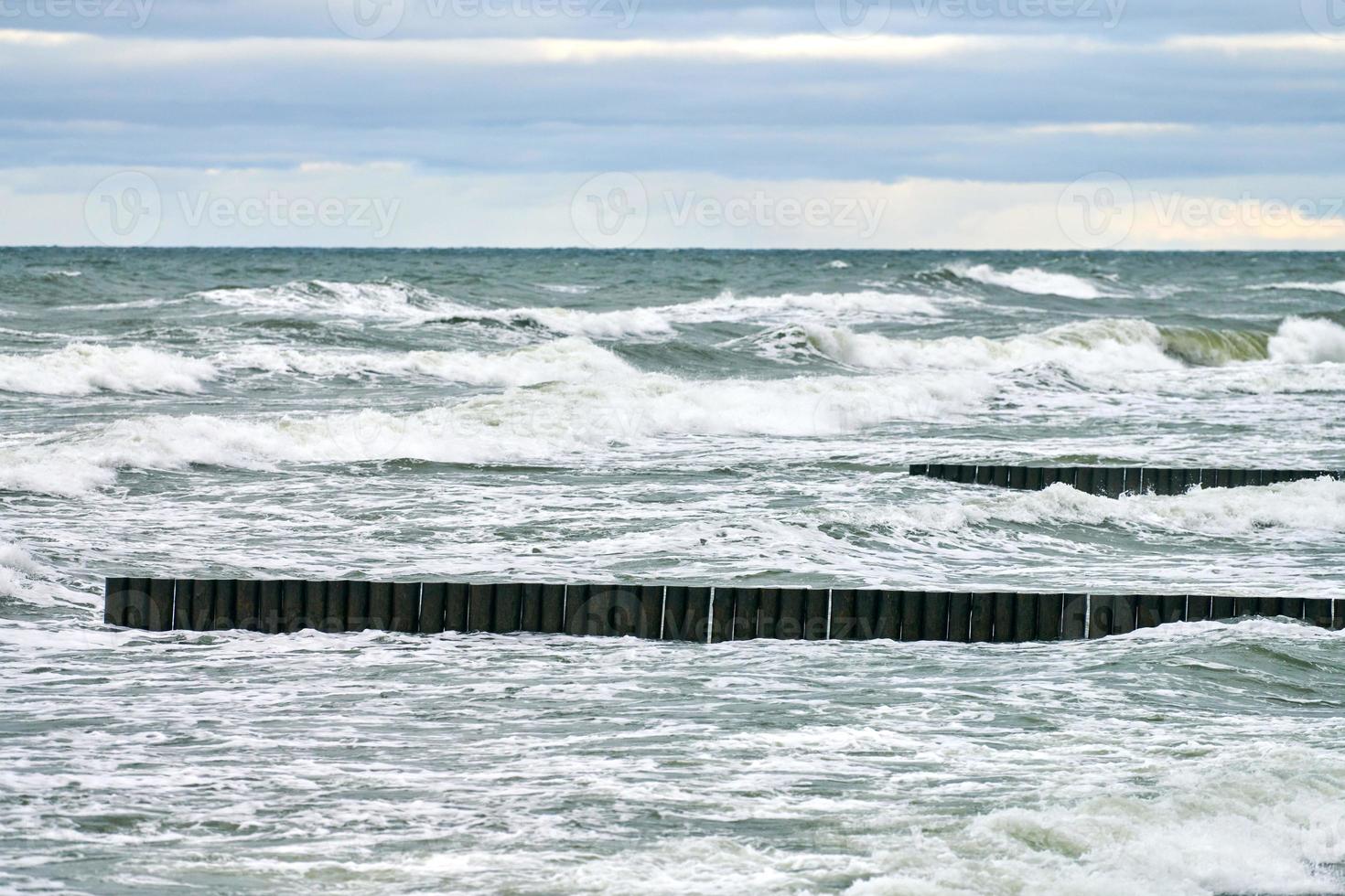 Blick auf das blaue Meer mit schäumenden Wellen und hölzernen Wellenbrechern foto