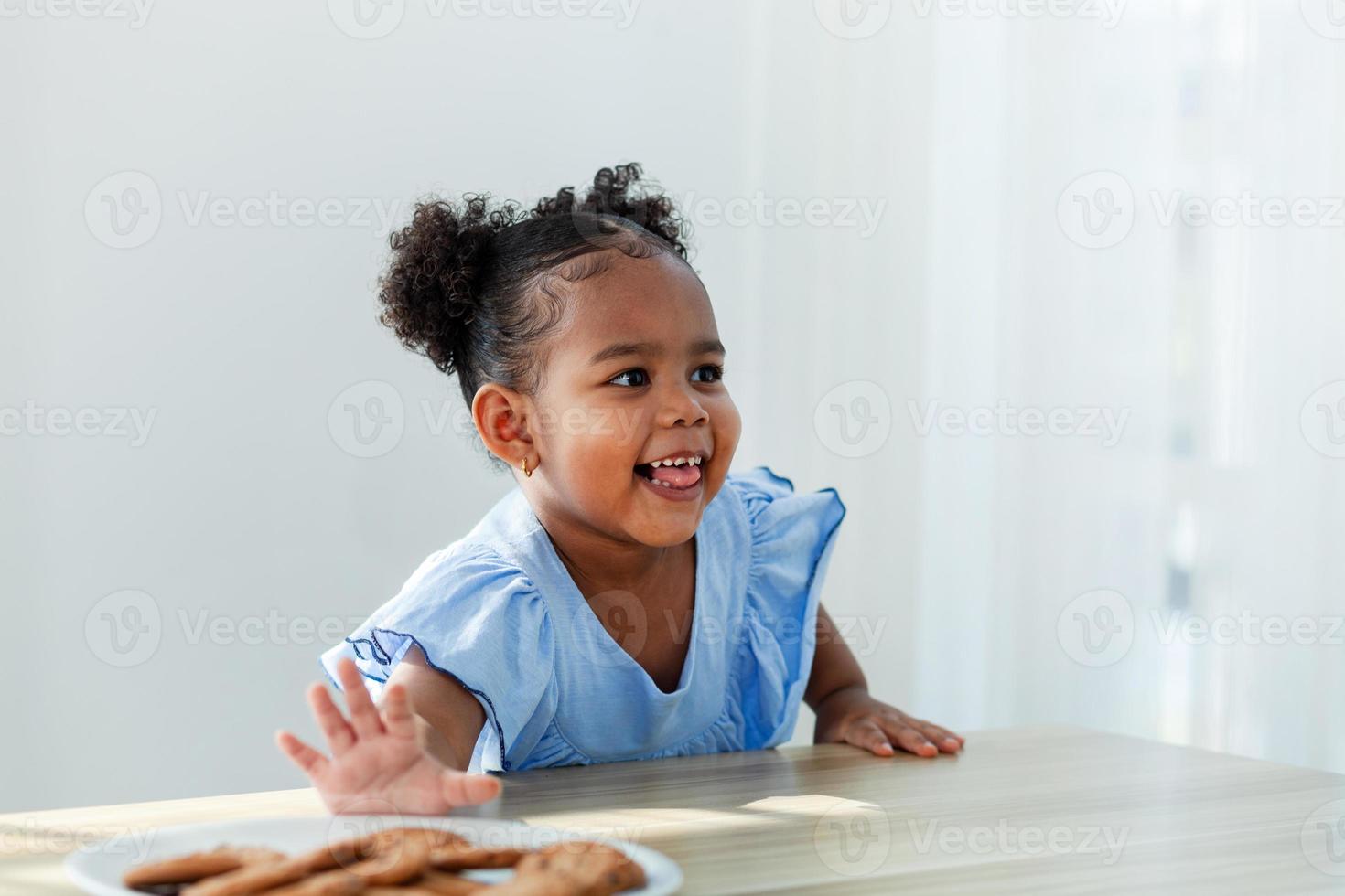 afroamerikanisches Mädchen, das Kekse isst, drückt Angst vor der Stille aus. während ihre Eltern kochen. foto