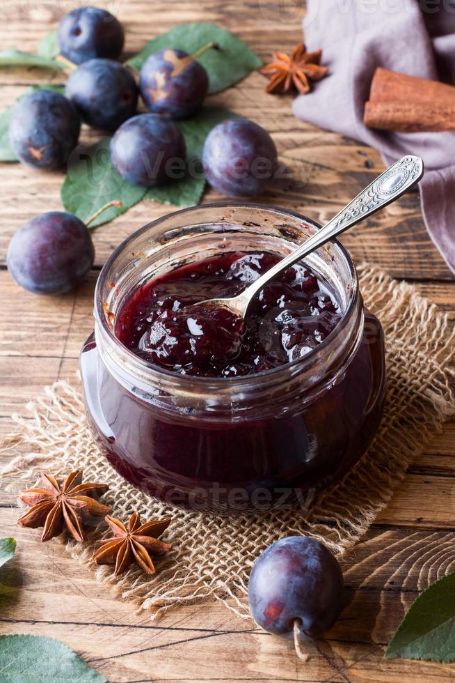 Pflaumenmarmelade in einem Glasgefäß. frische Pflaumenfrüchte auf einem Holztisch. foto