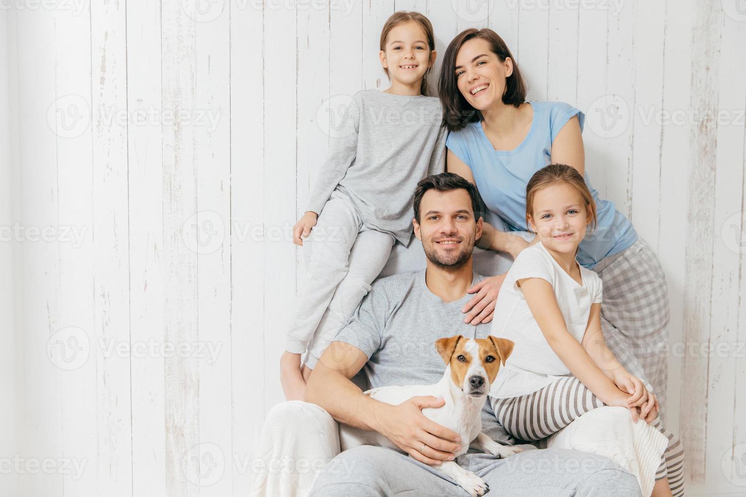 Porträt der glücklichen Familie drinnen. hübscher vater hält hund, schöne brünette mutter und zwei töchter, haben spaß zusammen, posieren für familienalbum, verbringen zeit zusammen. menschen, beziehungskonzept foto