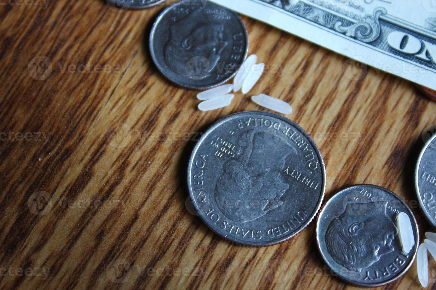 Dollarmünzen und Dollarscheine sind auf einem Holztisch mit Reiskörnern verstreut. foto