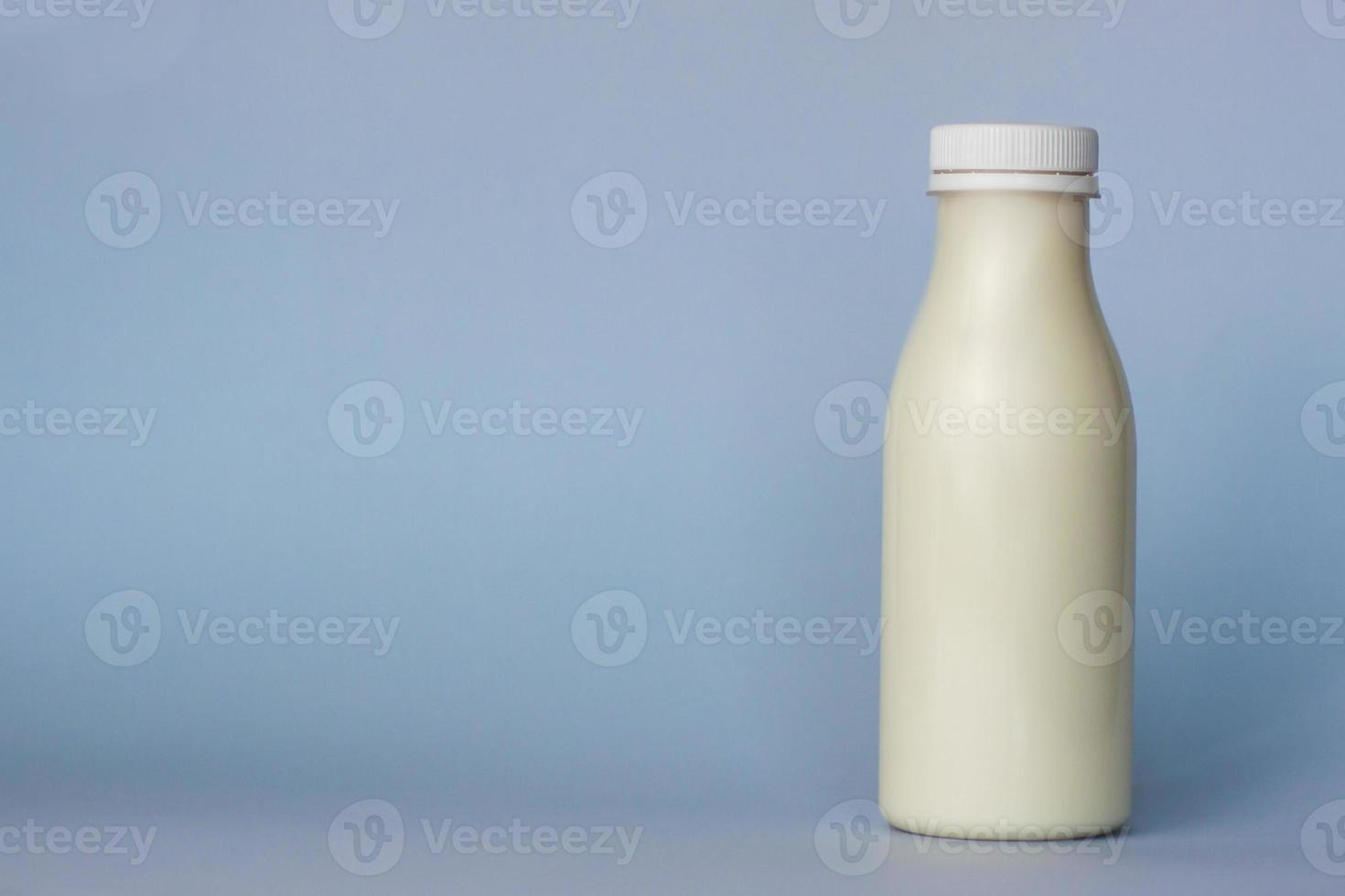 eine Flasche weiße Milch, hervorgehoben auf blauem Hintergrund, Nahaufnahme. foto