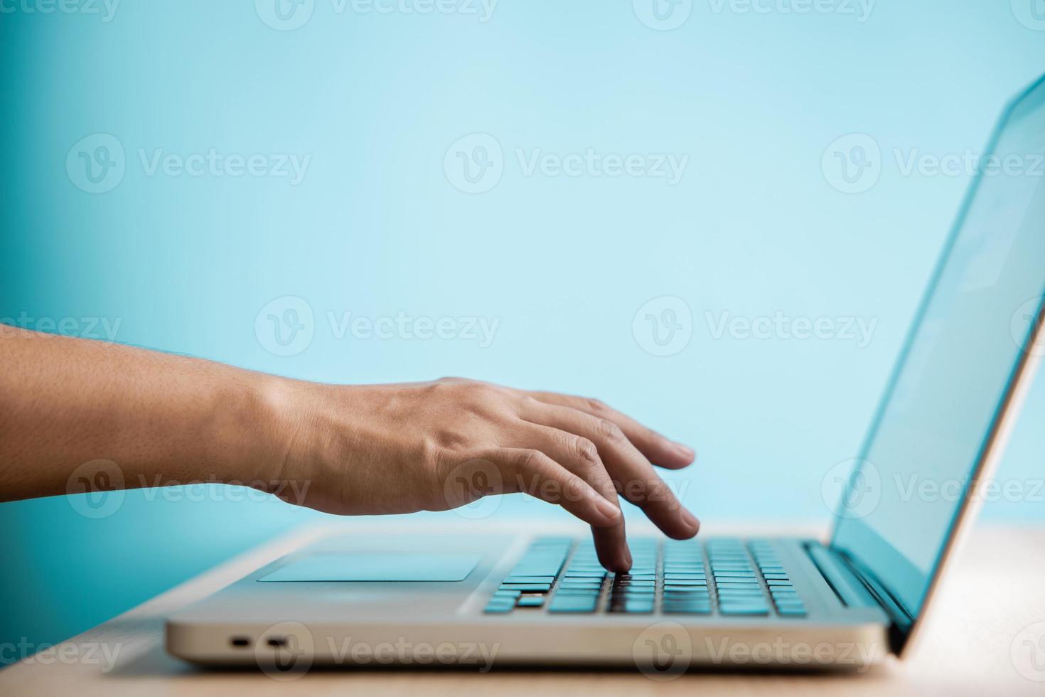 hand drücken computertastatur. Seitenansicht. Nahaufnahme und selektiver Fokus auf Finger. person, die einen laptop zum arbeiten am schreibtisch an der blauen wand verwendet. sauberes und minimales Foto