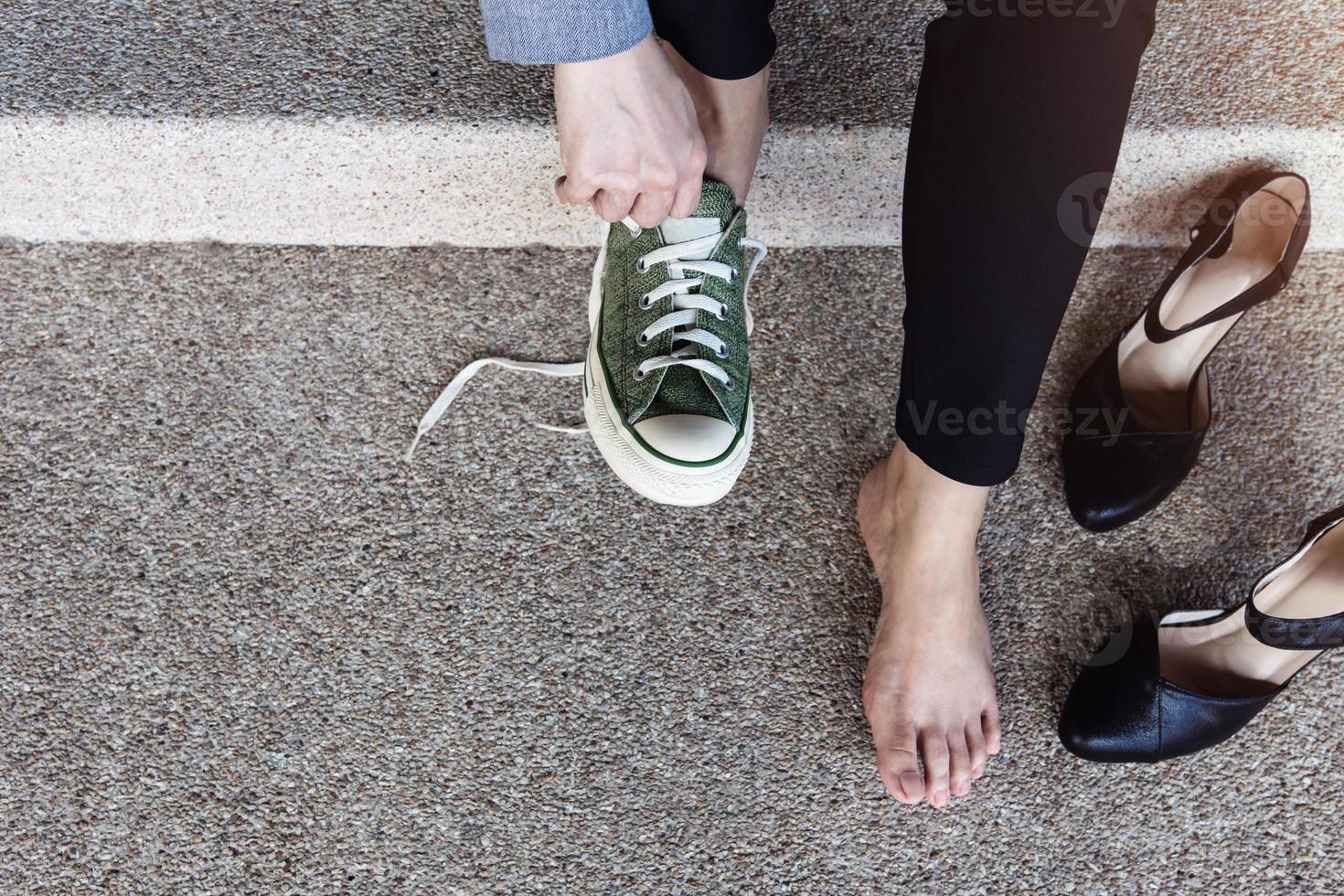 Gesundheitskonzept. barfüßige geschäftsfrau, die auf der treppe sitzt, um die schuhe von high heels zu bequemen sneakern zu wechseln. Ansicht von oben foto