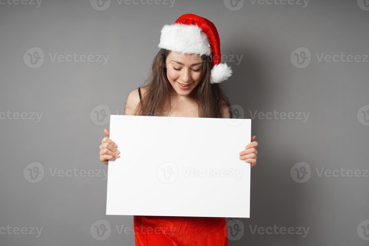 weiblicher Weihnachtsmann, der auf ein leeres Schild mit Kopierraum blickt foto