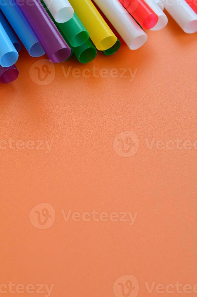 viele bunte strohhalme für getränke liegen auf einer leuchtend orangefarbenen hintergrundfläche foto