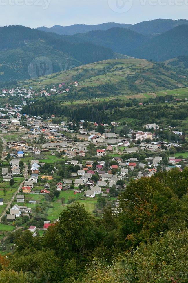 eine schöne aussicht auf das dorf mezhgorye, karpatengebiet. Viele Wohngebäude, umgeben von hohen Waldbergen und einem langen Fluss foto