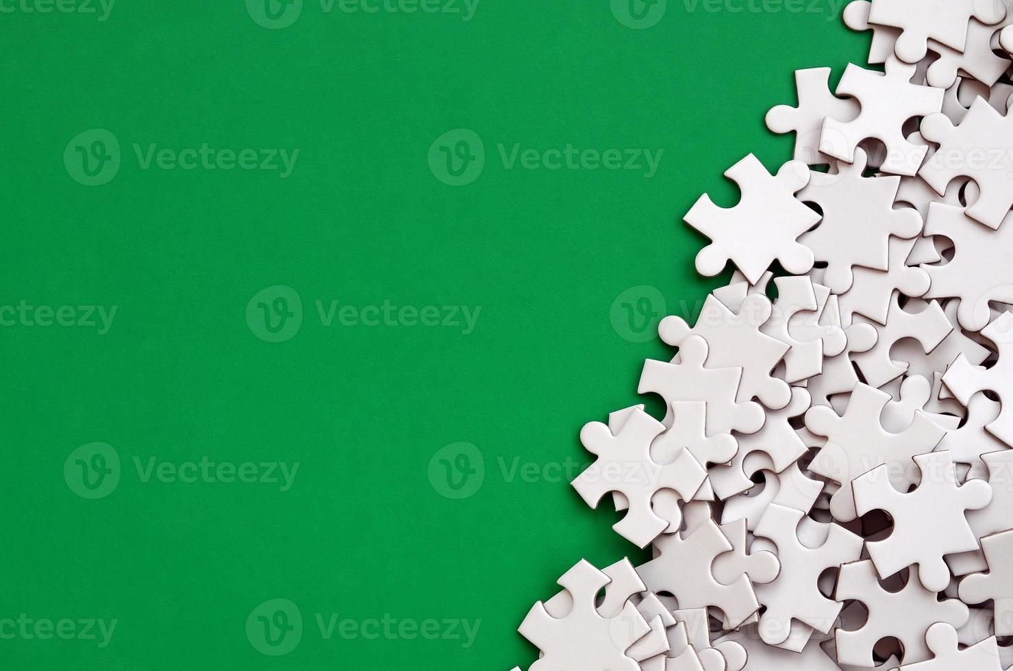 Ein Haufen ungekämmter Elemente eines weißen Puzzles liegt auf dem Hintergrund einer grünen Oberfläche. texturfoto mit kopierraum für text foto