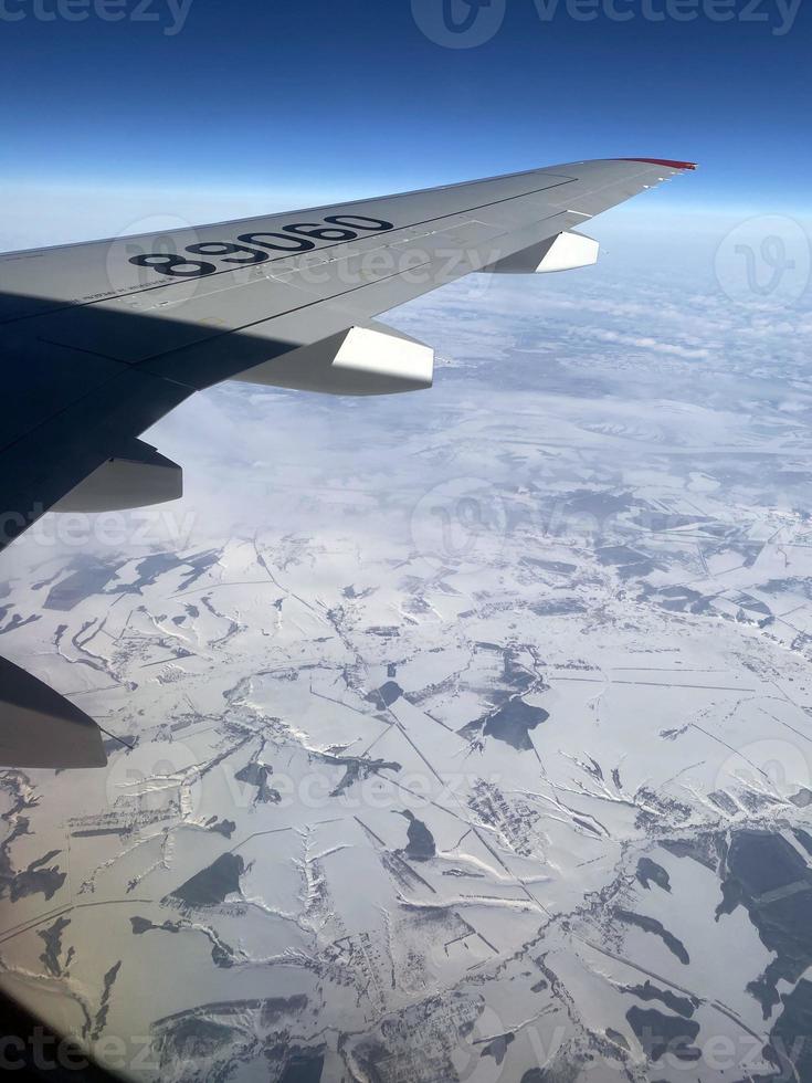 Blick aus dem Flugzeugfenster. Auf dem Foto der Blick aus dem Fenster, die Tragfläche des Flugzeugs, Berge, Schnee.