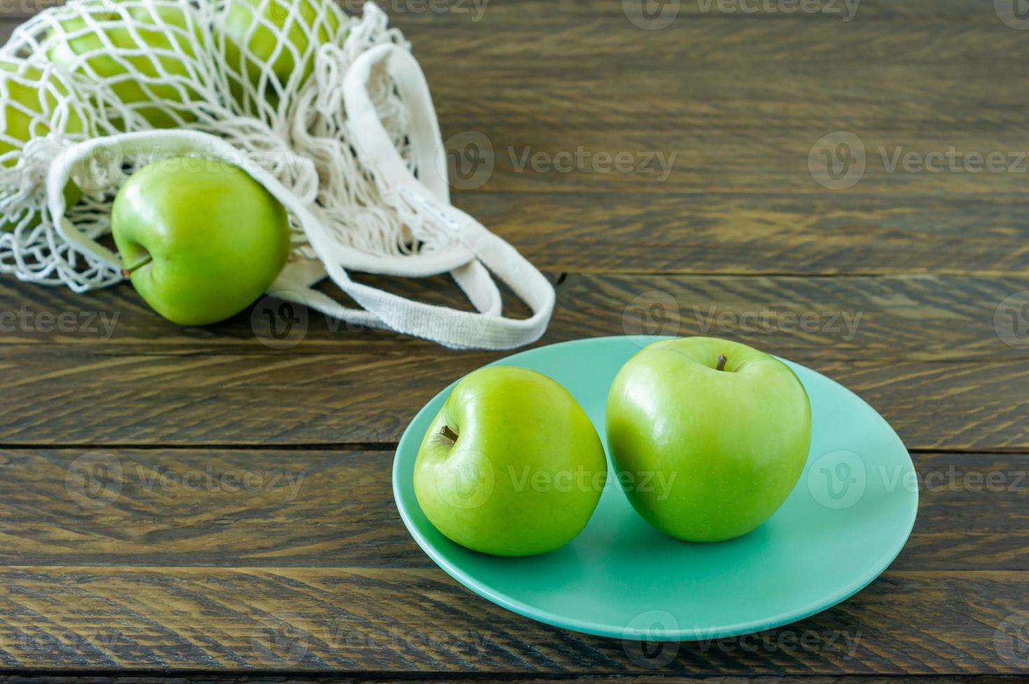 Bio-Oma-Smith-Äpfel auf einem Teller mit Mesh-Textiltasche auf Holztisch. foto