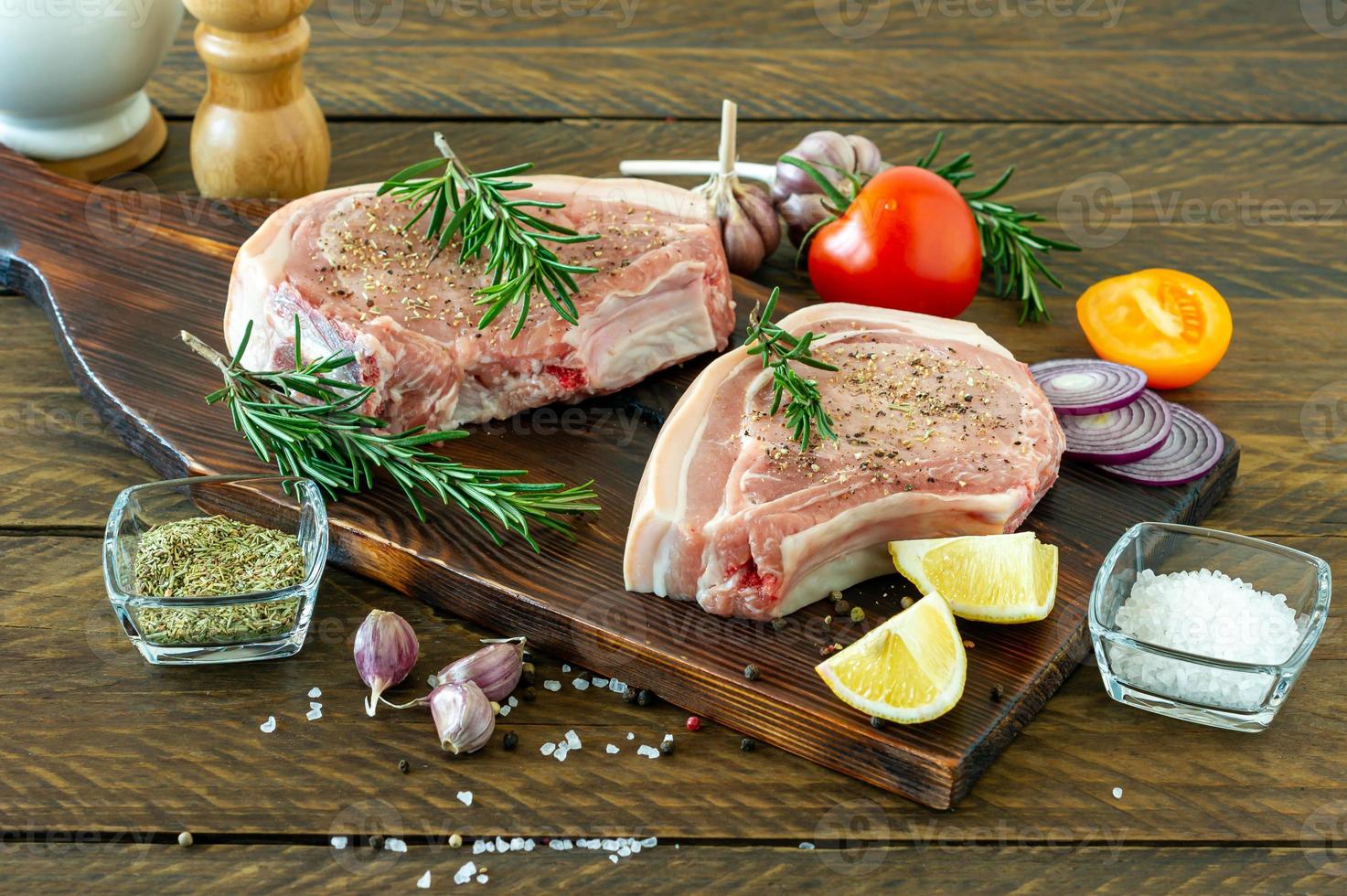 Stücke rohes Schweinesteak mit Gewürzen und Kräutern Rosmarin, Salz und Pfeffer auf Holzbrett auf Holzhintergrund im rustikalen Stil foto