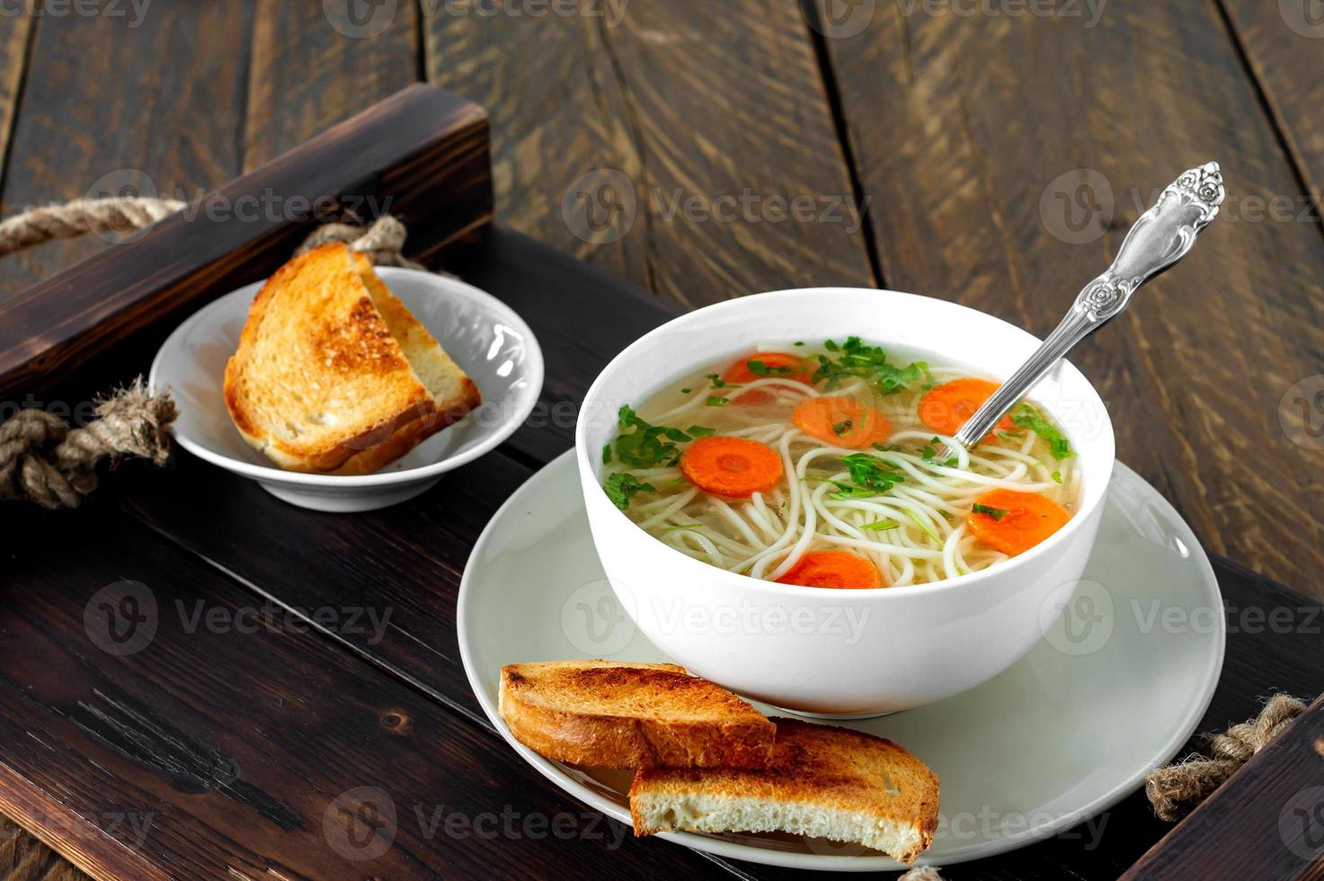 frische Bouillon in einer weißen Schüssel mit fein gehackten Kräutern mit Petersilie und Knoblauch auf einem Holztisch. scharfe Suppe aus Hühnerfleisch, Karotten, Zwiebeln, Knoblauch, Petersilie und Pfeffer. foto