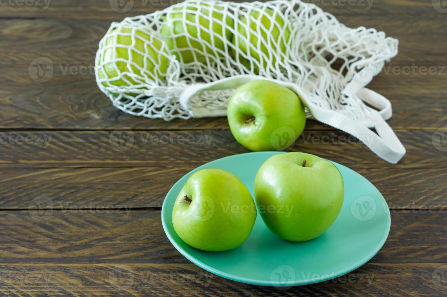 Bio-Oma-Smith-Äpfel auf einem Teller mit Mesh-Textiltasche auf Holztisch. foto
