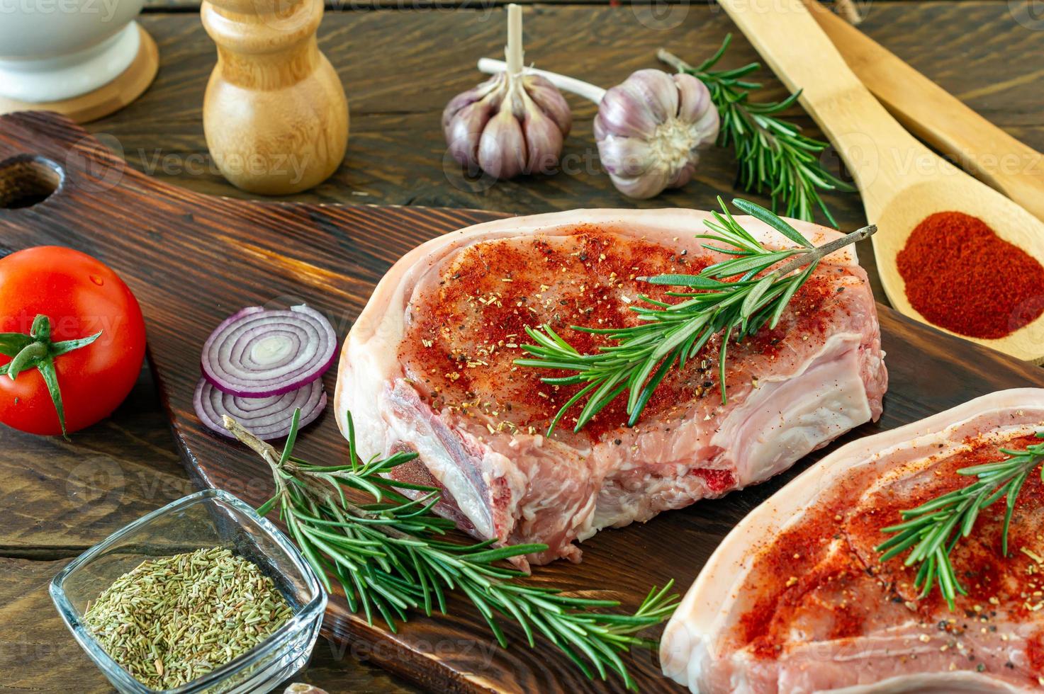 Stücke rohes Schweinesteak mit Gewürzen und Kräutern Rosmarin, Salz und Pfeffer auf Holzbrett auf Holzhintergrund im rustikalen Stil. foto