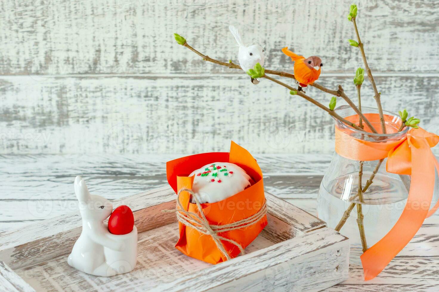 osterfrühlingskomposition mit bemalten eiern, keramikhäschen und kleinen vögeln auf zweigen. festliche dekoration für die osterfeiertage mit leckerem osterkuchen oder kulitch foto