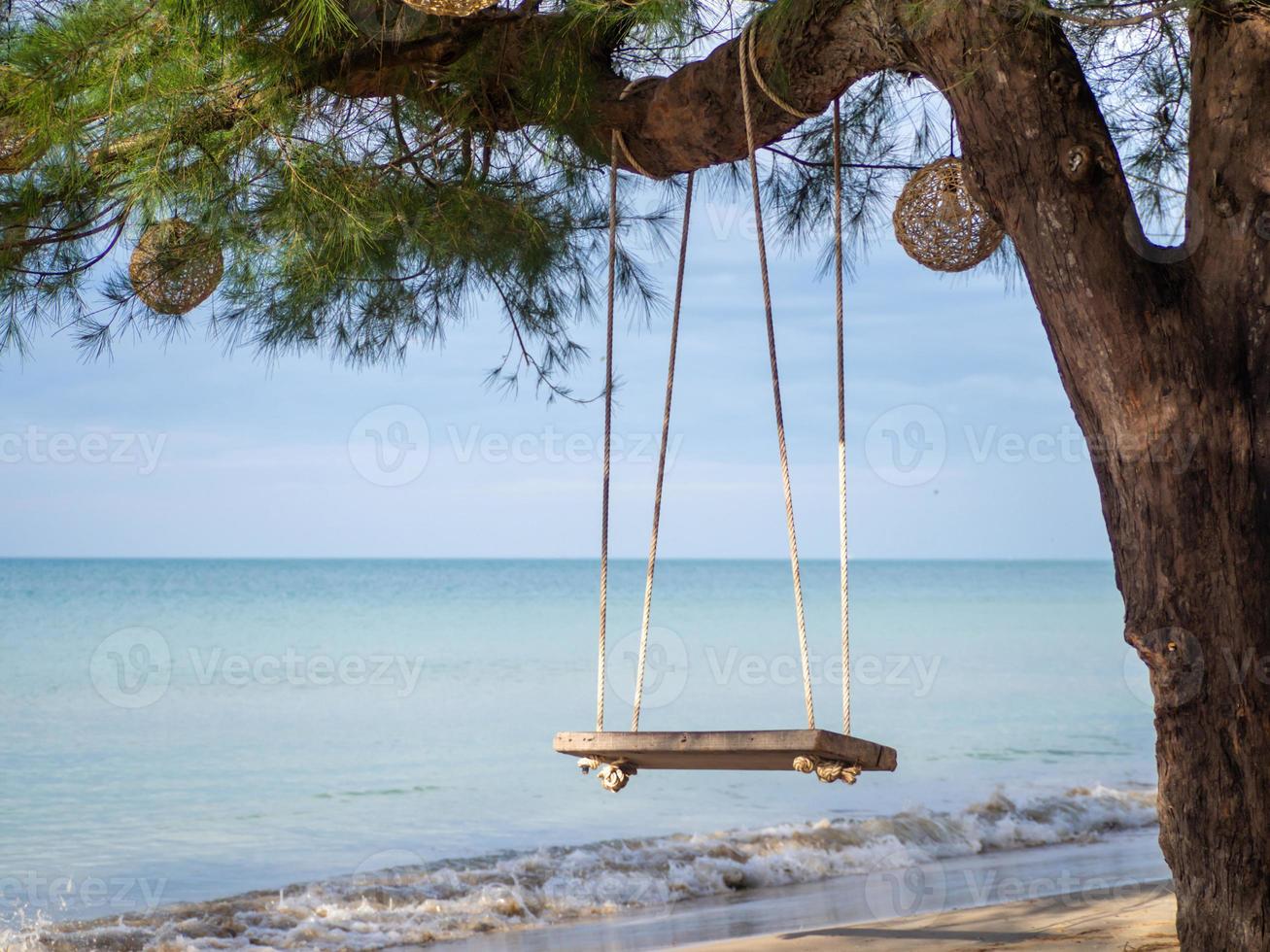 Holzschaukel, die am Baum im Hintergrund hängt, ist ein blaues Meer. foto