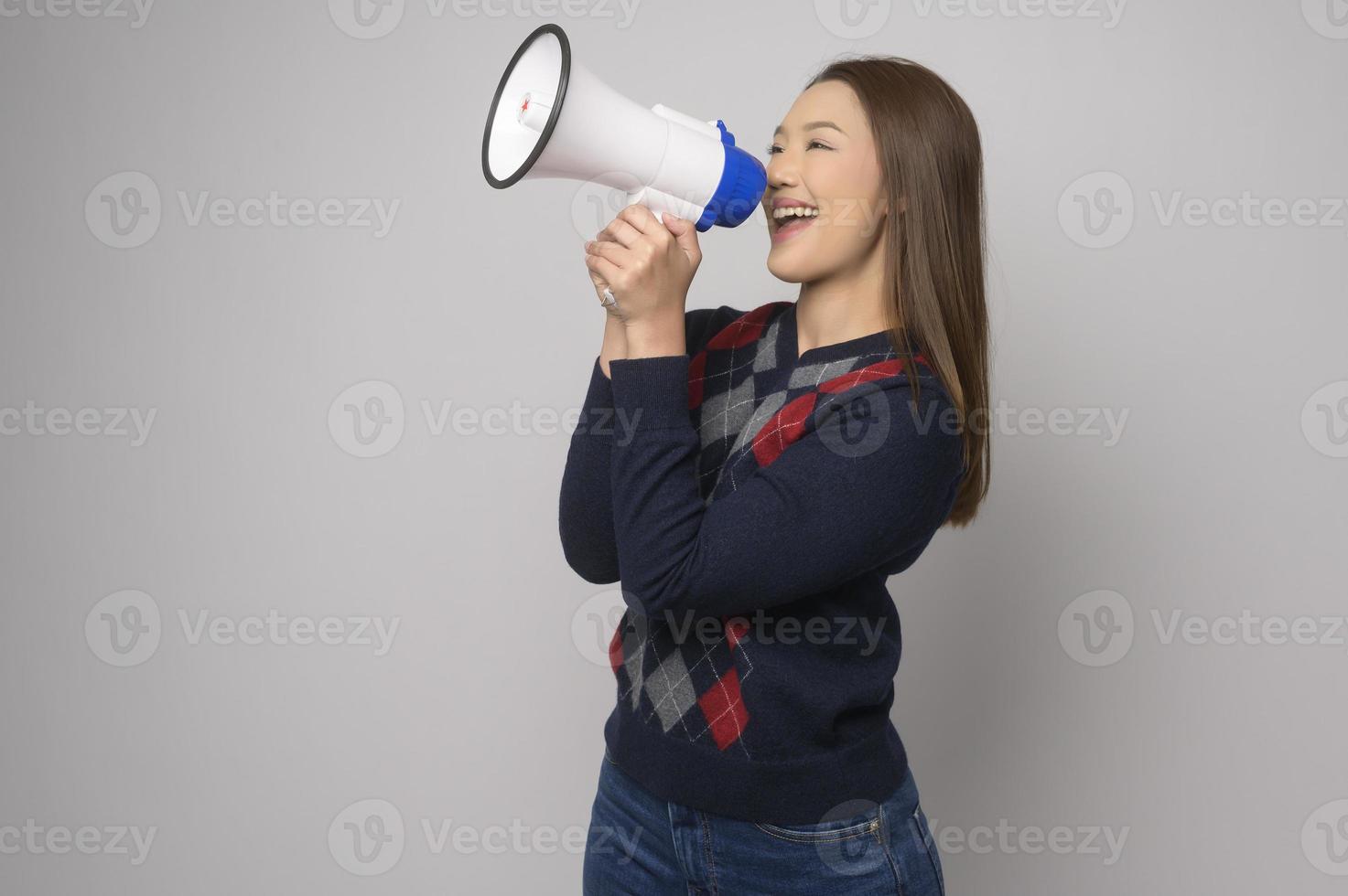 junge lächelnde Frau, die Megaphon über weißem Hintergrundstudio hält. foto