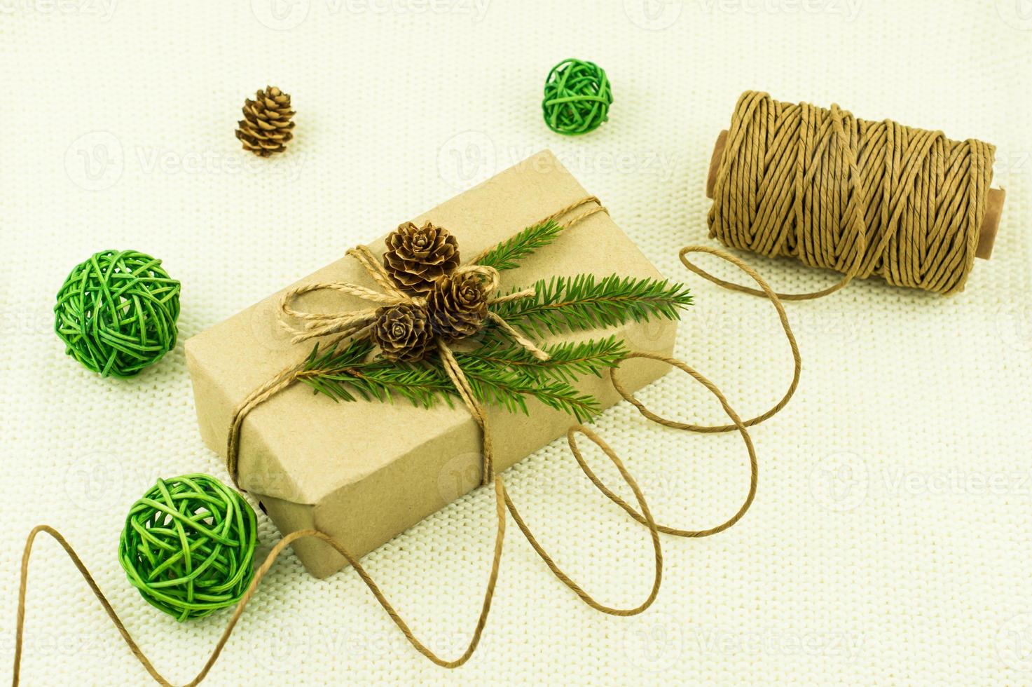 Neujahrsfeiertagsbox mit einem Geschenk, das mit Ihren eigenen Händen dekoriert und in Kraftpapier eingewickelt ist. grüne Fichtenzweige, Zapfen, Zierkugeln. foto