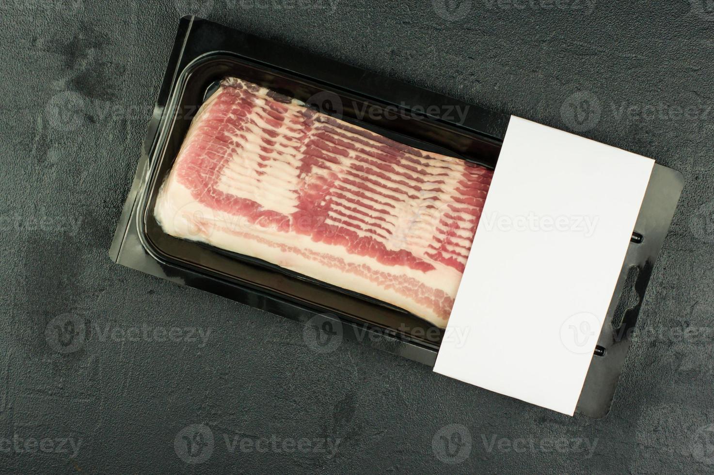 geräucherter Schweinefleischspeck in werkseitiger Kunststoffverpackung auf schwarzem Hintergrund. Ansicht von oben. Logo-Layout-Design. foto