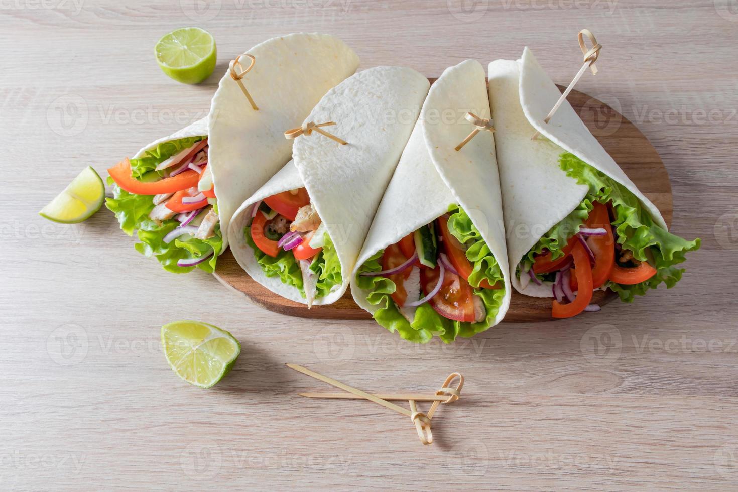 Vorderansicht von saftigen hausgemachten Burittos in einem Fladenbrot mit Gemüse und Hähnchenfilet. hölzerner heller hintergrund. foto