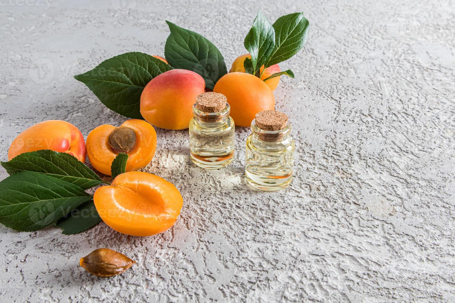 Zwei Glasflaschen mit Korkverschluss mit Aprikosenkernöl zwischen Früchten und saftigen Aprikosenblättern. grauer Zementhintergrund. eine Kopie des Raums. foto