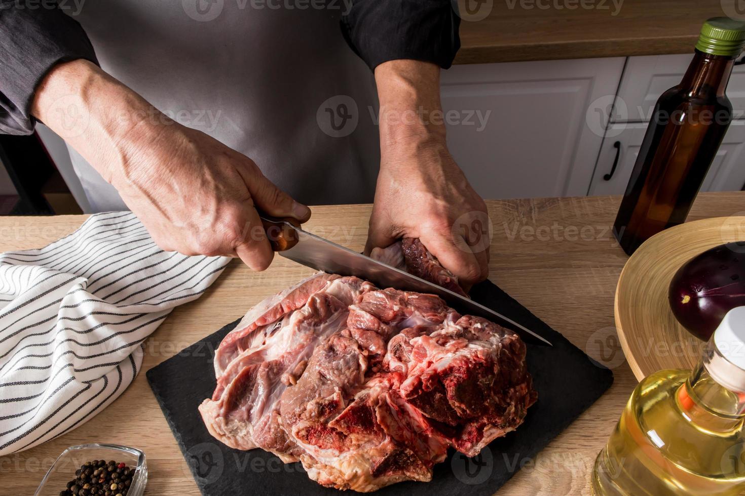 Die Metzgerhände schneiden auf einer Schieferplatte und einem Holztisch mit einem scharfen Kochmesser ein frisches Stück Rindfleisch. Öko-Produkte aus eigener Landwirtschaft. foto