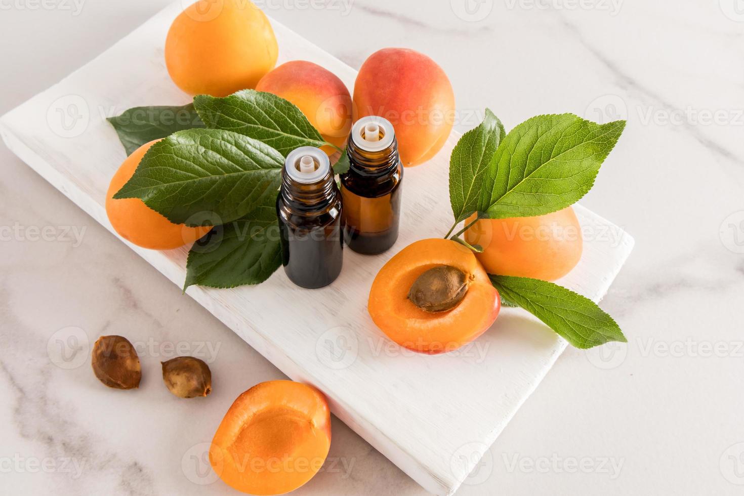 Zwei medizinische Flaschen mit natürlichem ätherischem Aprikosenöl auf einem weißen Holzpodium mit Früchten. das Konzept der Verjüngung, Beruhigung und Entspannung. foto