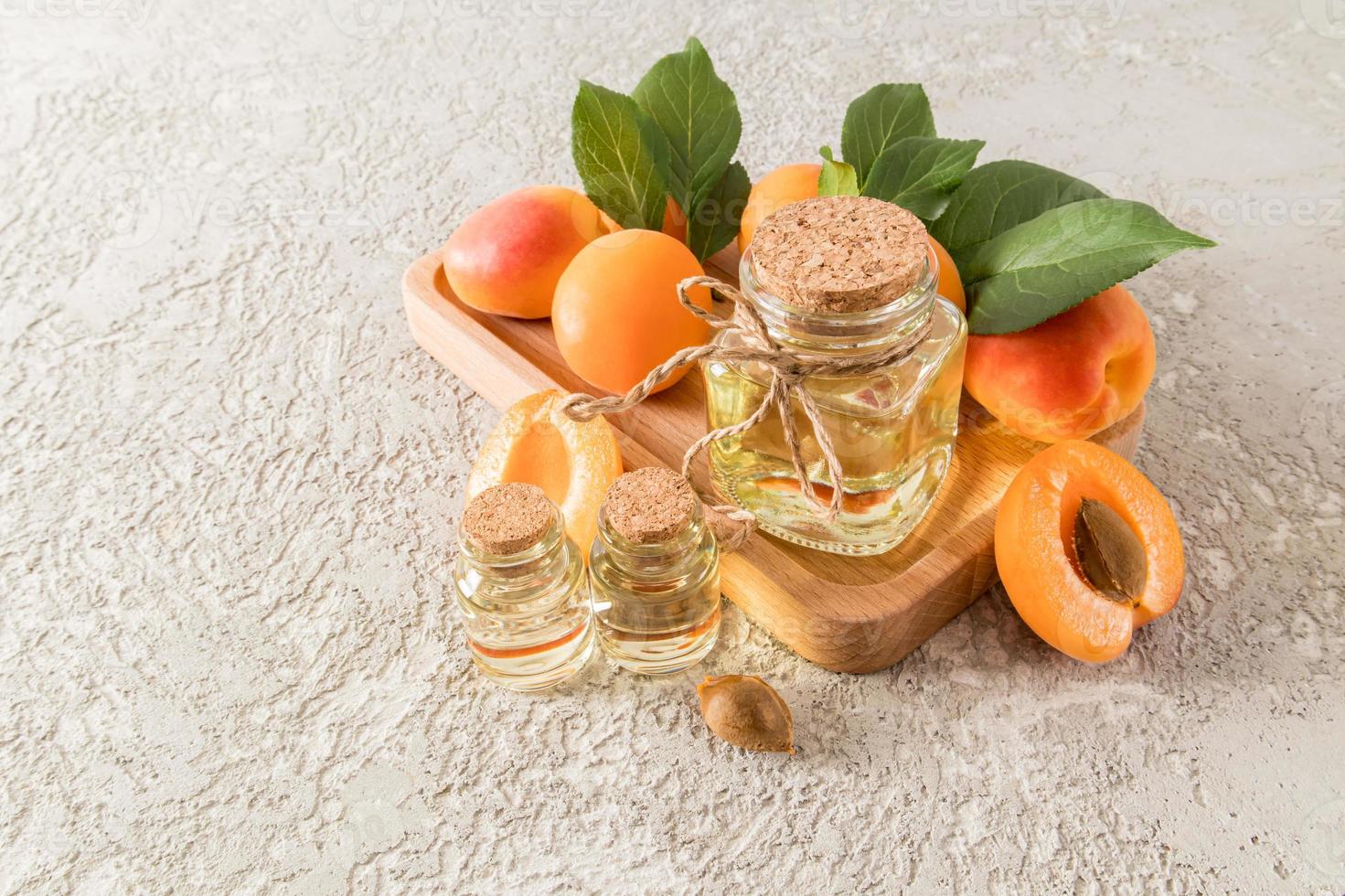 Flasche Aprikosenkernöl auf einem Holztablett mit reifen Früchten und grauem Zementhintergrund. eine Kopie des Raums. Bio-Hautpflege. foto