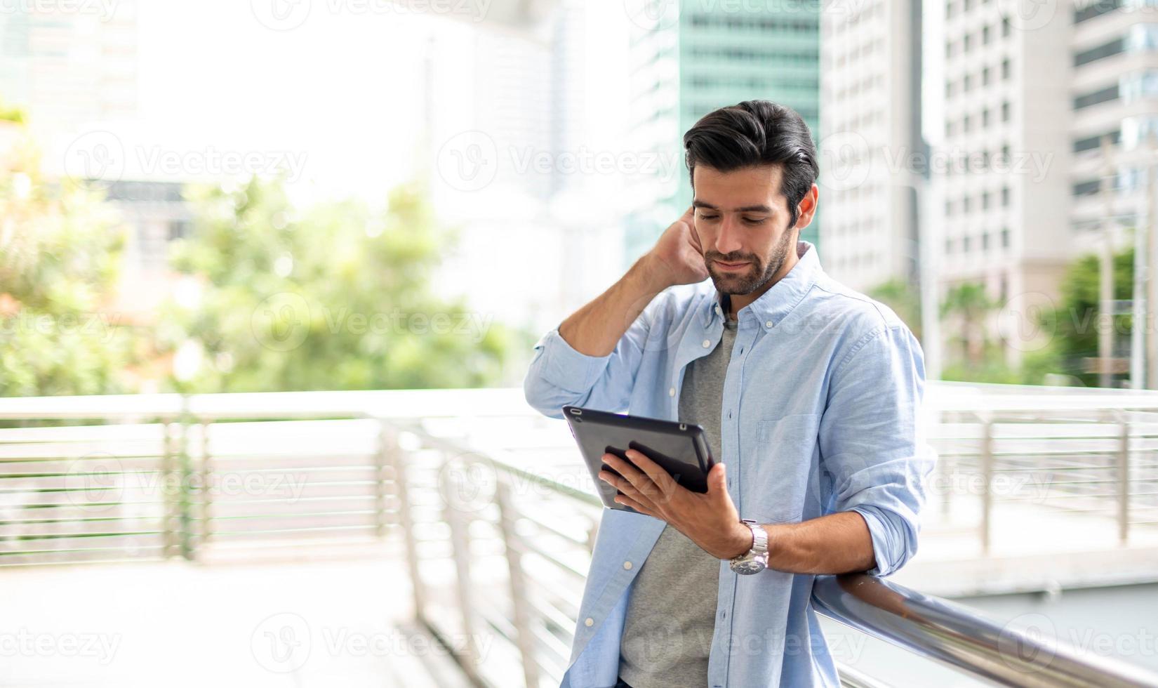 der junge mann, der ein tablet benutzt, um außerhalb des büros zu arbeiten. der mann, der lässige kleidung trägt und sich nachdenklich und ernst fühlt. foto