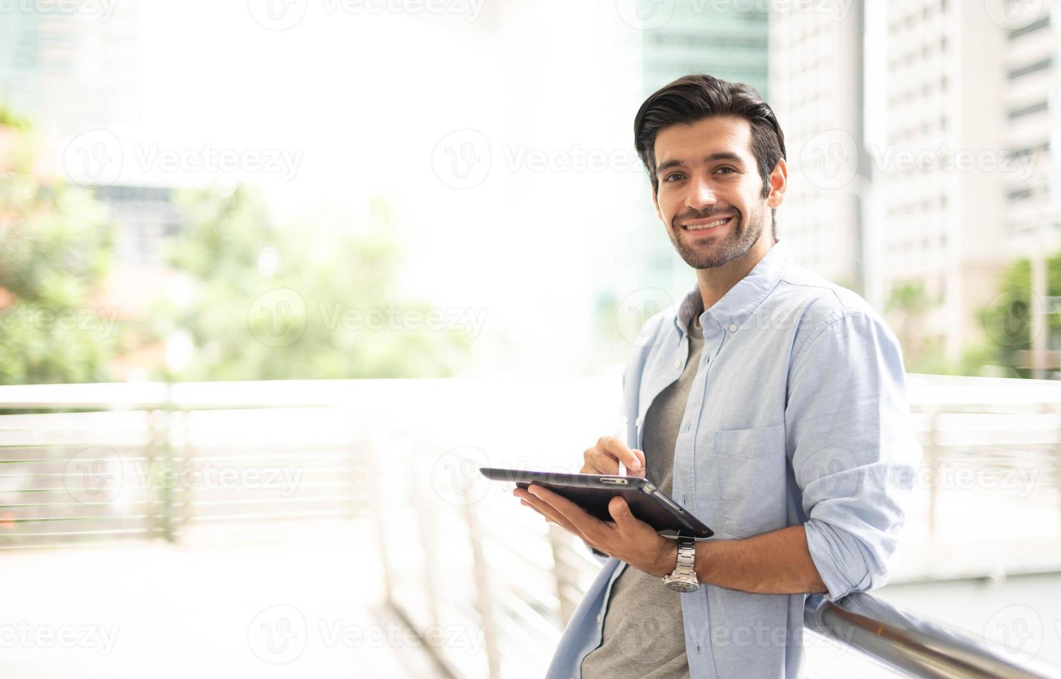 der junge mann, der ein tablet benutzt, um außerhalb des büros zu arbeiten. der mann, der lässige kleidung trägt und sich entspannt und glücklich fühlt. foto