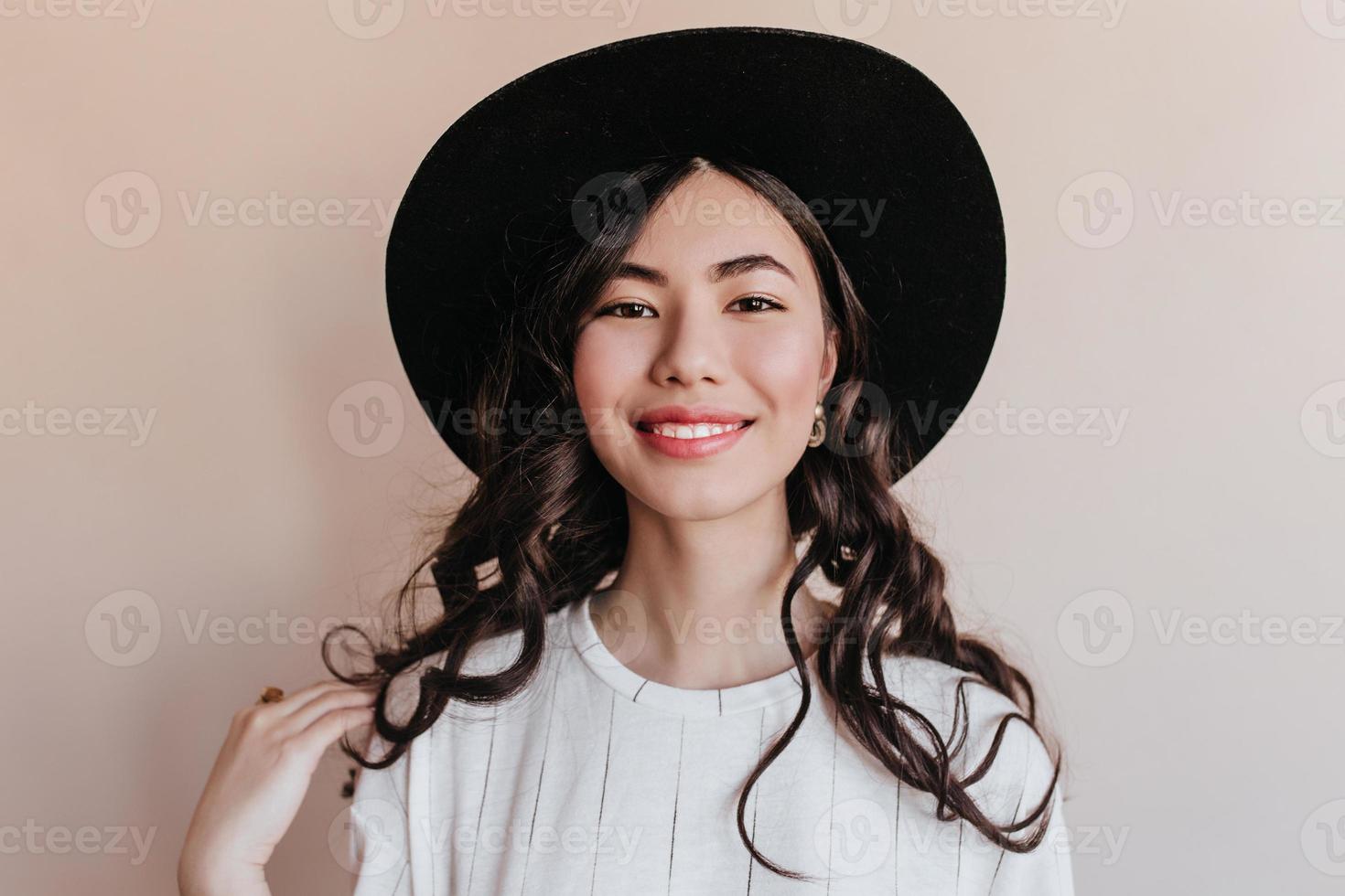 Vorderansicht der fröhlich lächelnden Asiatin. Studioaufnahme eines glücklichen koreanischen Mädchens mit schwarzem Hut. foto